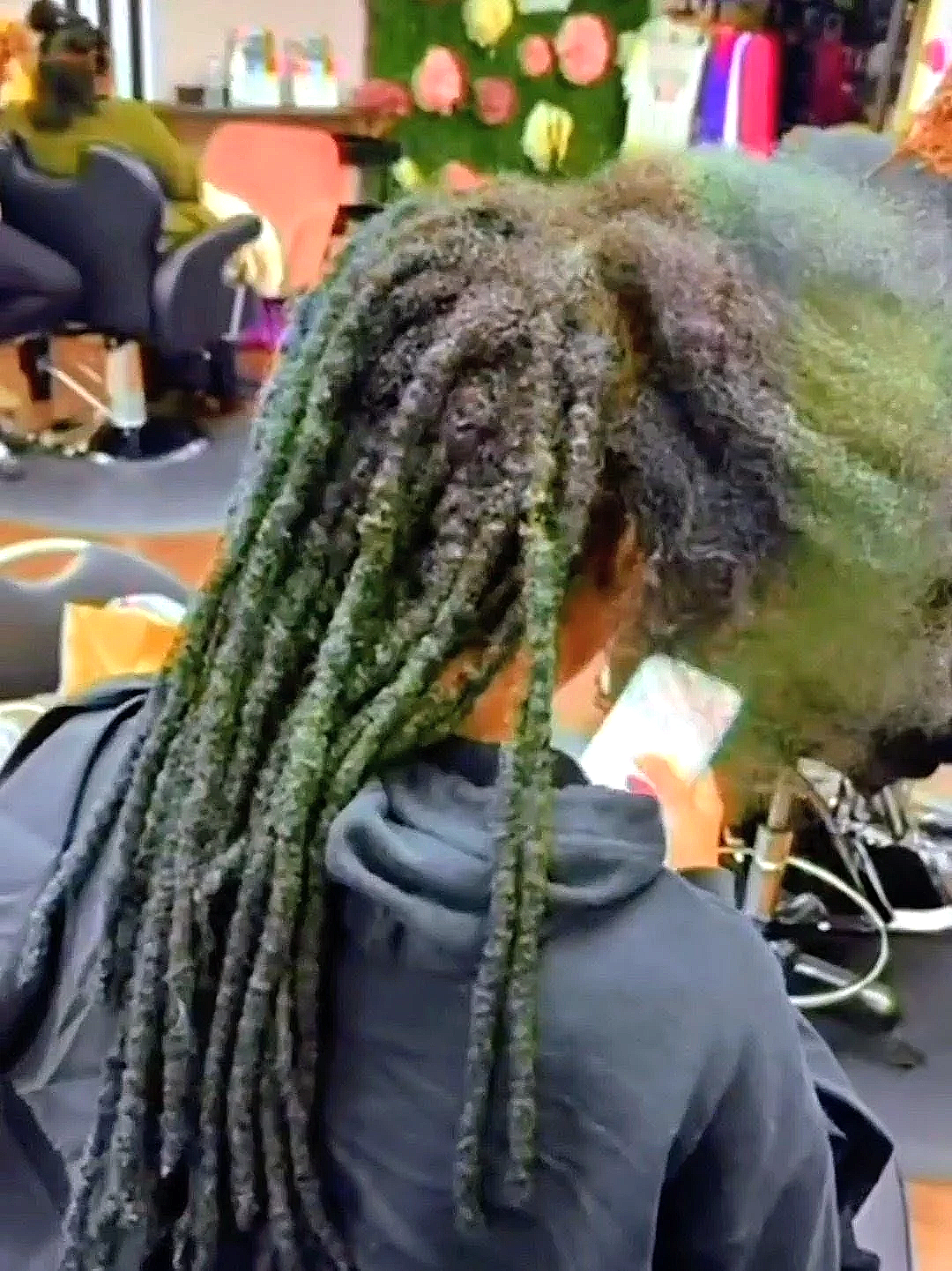 A person with long dreadlocks standing inside a store with colorful decorations and people shopping.