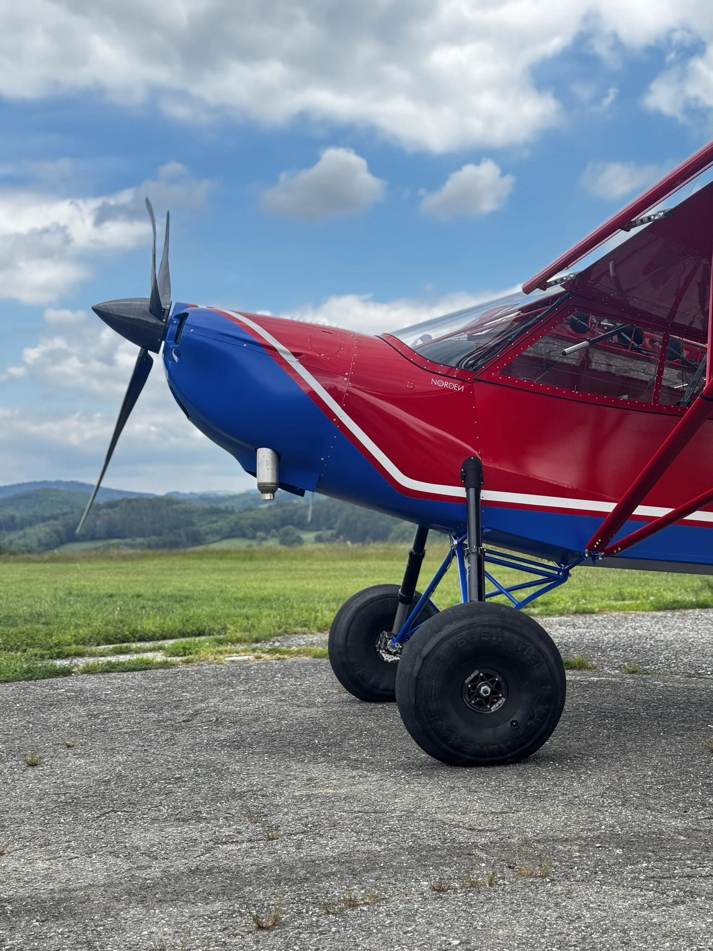 A blue and black single-engine light aircraft flying in cloudy skies.