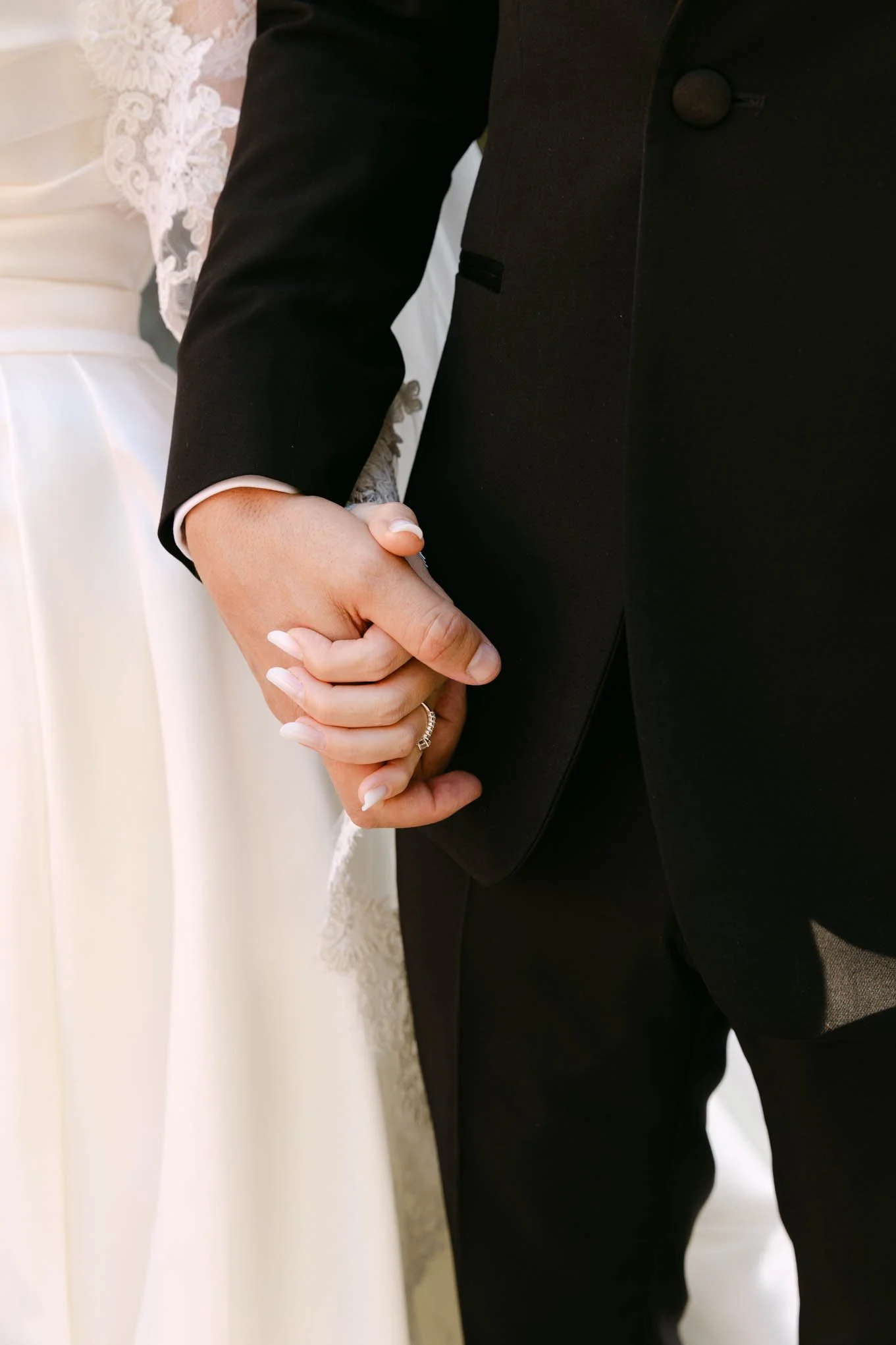 Close-up of a bride and groom holding hands during a wedding ceremony, with the bride wearing a wedding dress and the groom in a black suit. Vogue Style!