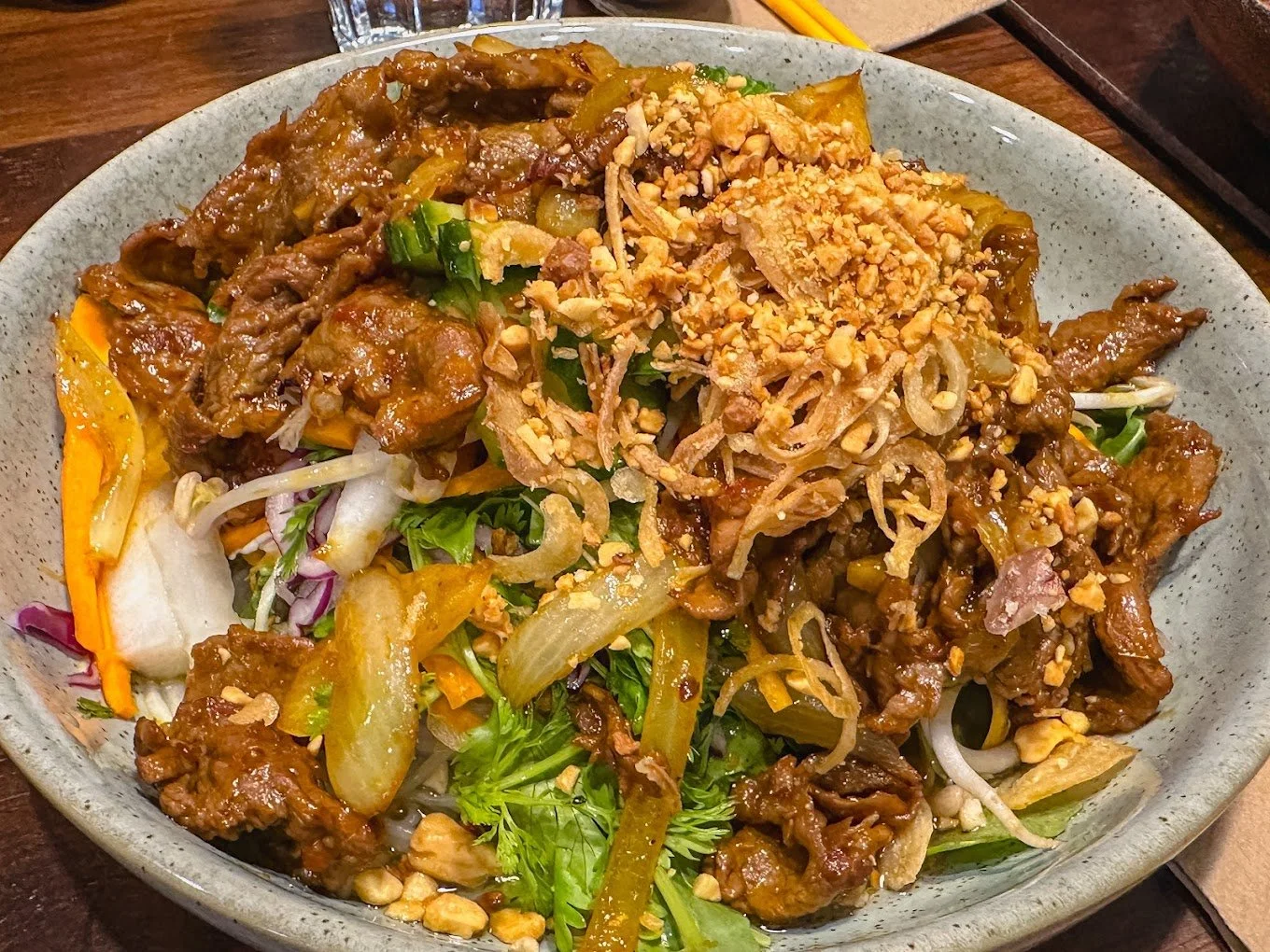 A bowl of Asian-style beef stir-fry with vegetables and crushed peanuts