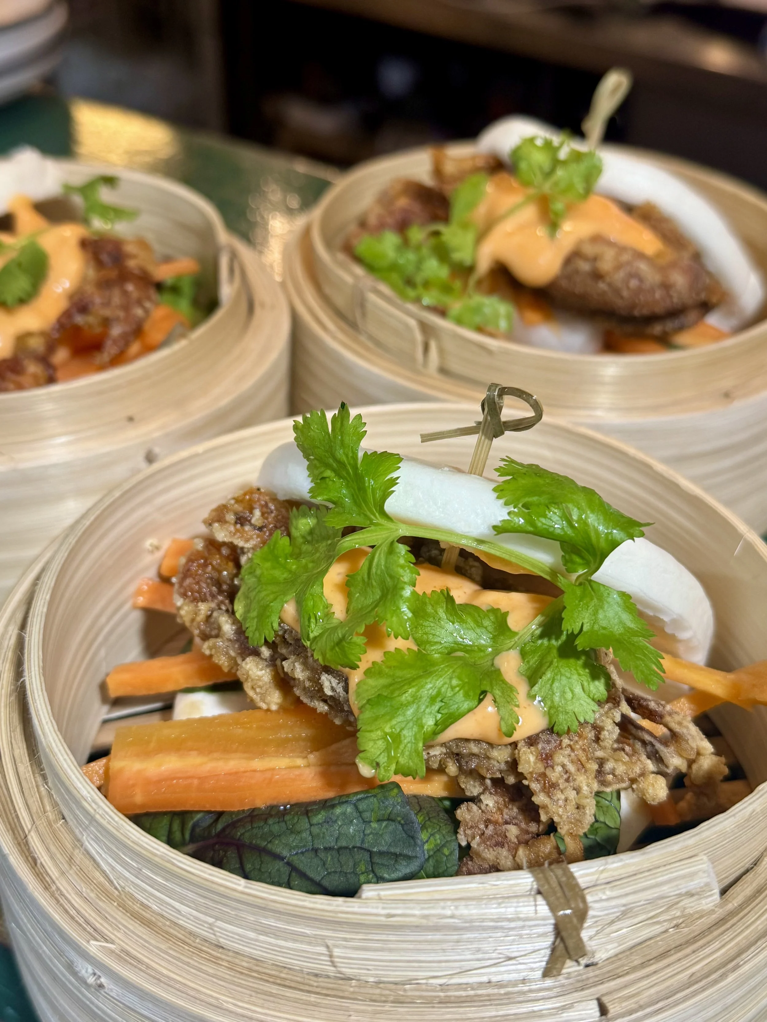 Close-up of Asian steamed dumplings served in bamboo steamers, garnished with fresh cilantro and vegetables.