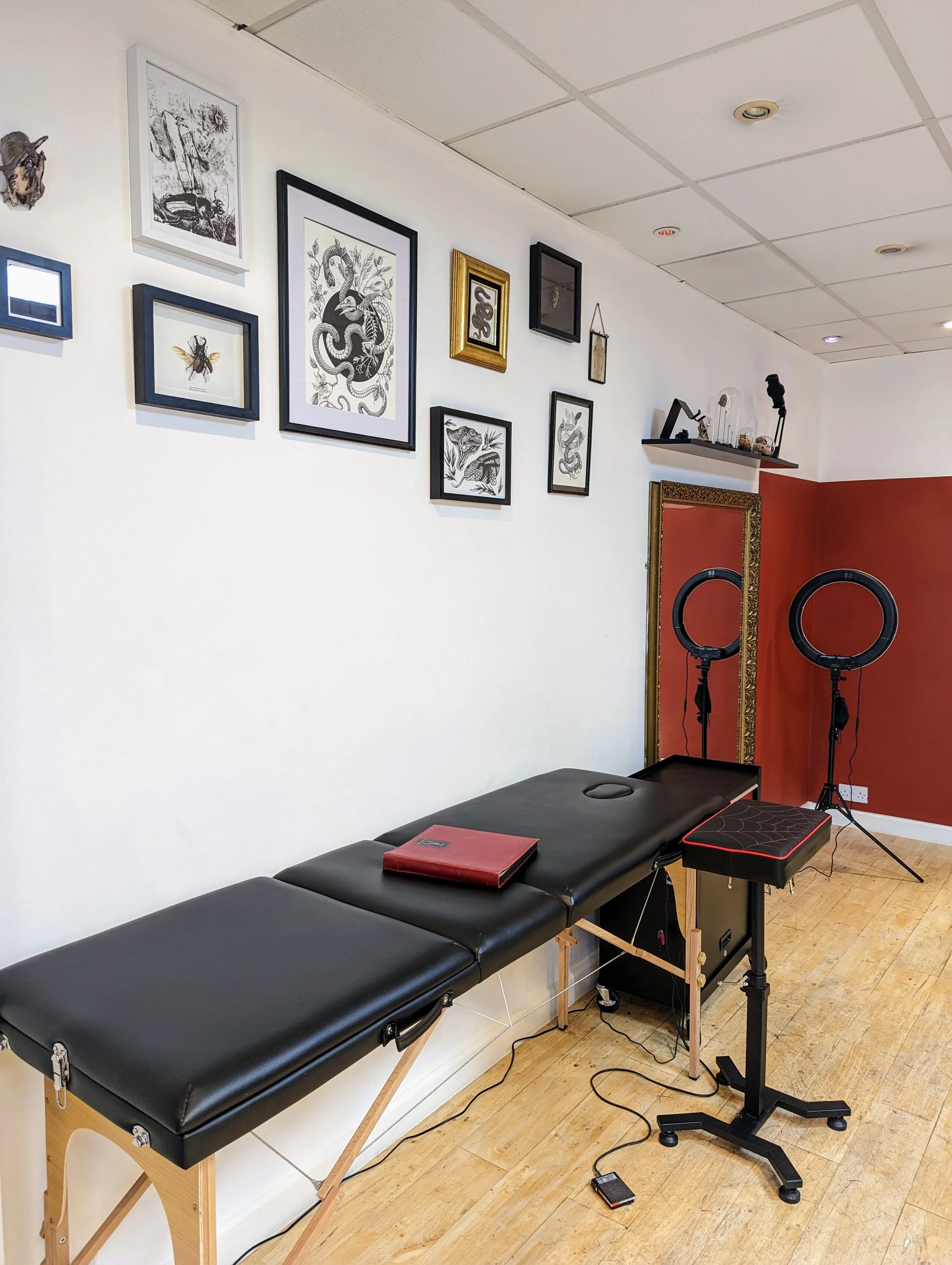 My previous studio arrangement, showing a white wall withe various pieces of framed art. My red flashbook is on my tattoo table, and my station and armrest are in view.