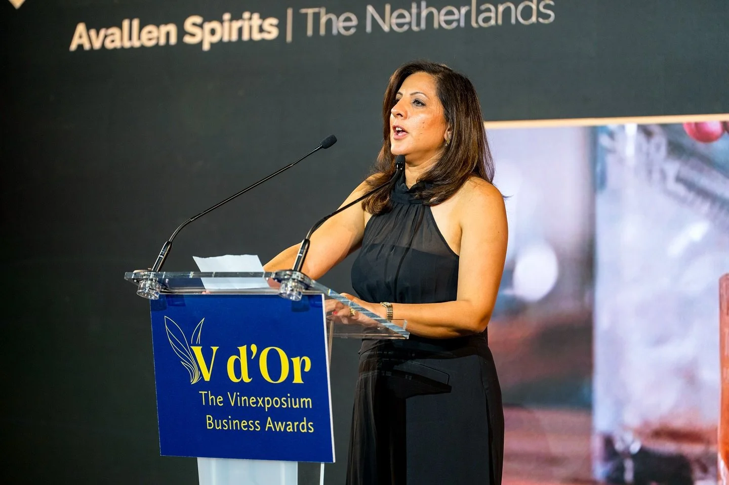 Woman speaking at a podium during the Vinexposium Business Awards event, with a backdrop reading 'Avallen Spirits | The Netherlands'.