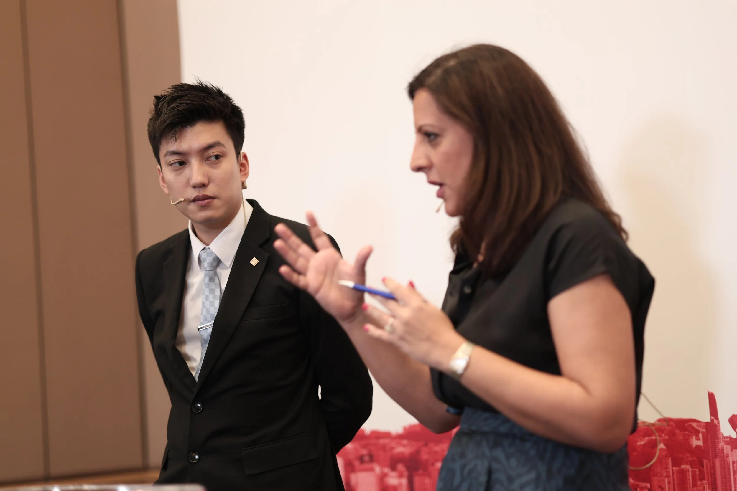 Nimmi Malhotra and a young man in a professional setting, with the woman speaking and gesturing while the young man listens attentively.
