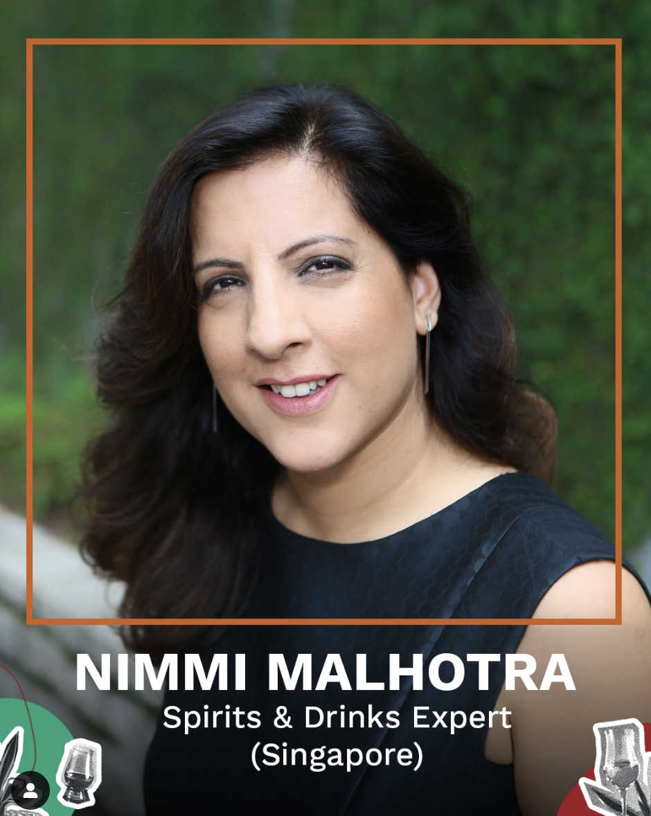 Photograph of Nimmi Malhotra, a Spirits & Drinks Expert from Singapore, smiling with long dark hair and wearing a black sleeveless top, standing outdoors with a blurred green background.