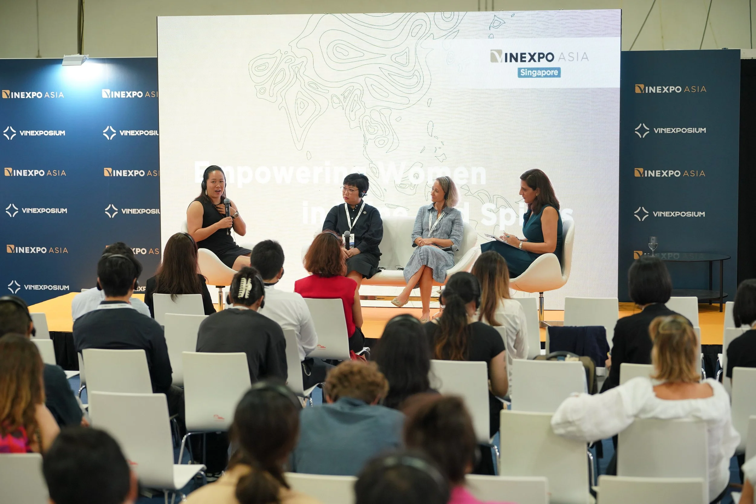 Panel discussion at INEXPO Asia in Singapore with four women on stage, three seated and one speaking during a conference titled "Empowering Women" with an audience of diverse attendees in front.