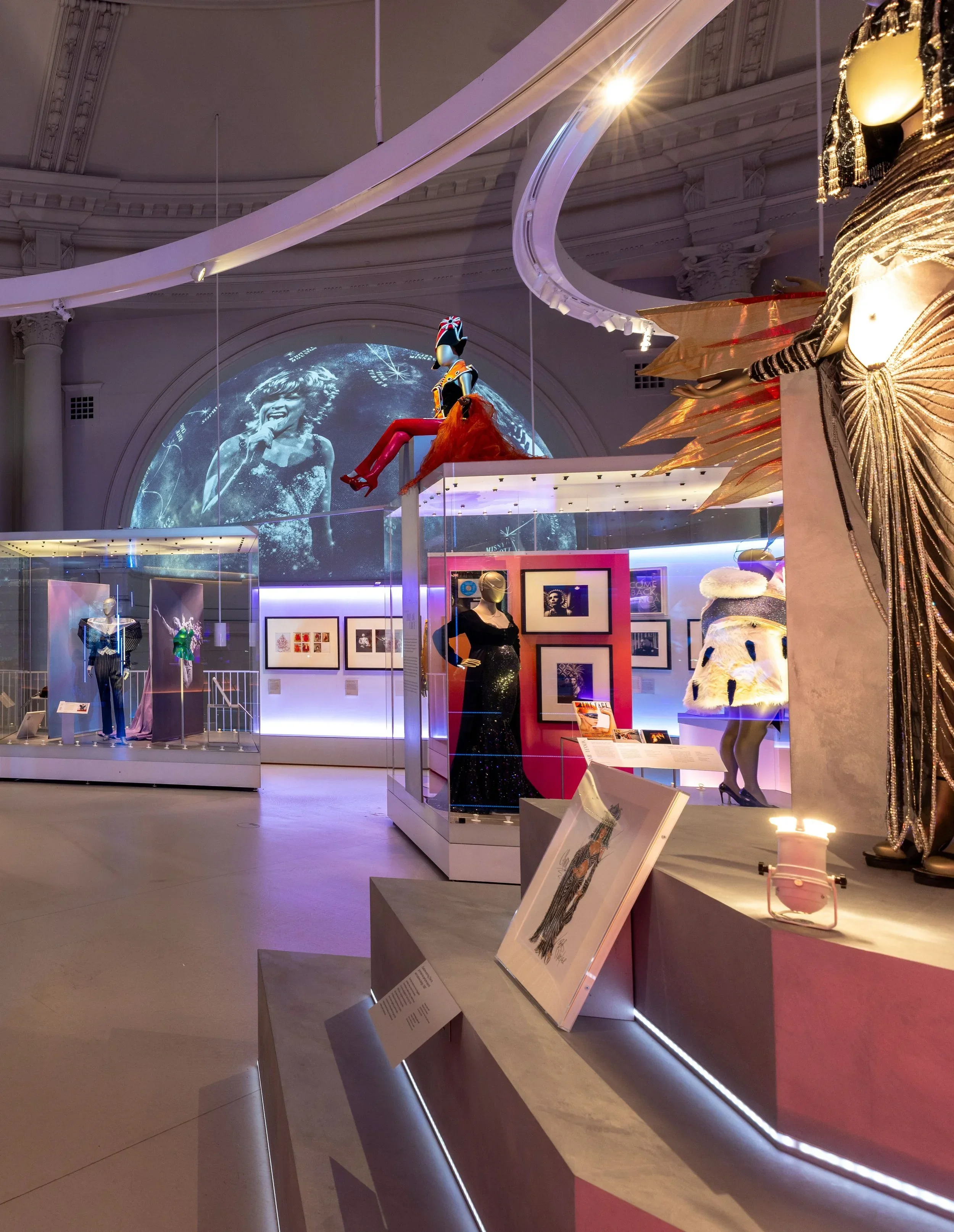 Exhibit with fashion mannequins, stylized costumes, and framed photographs in an art gallery.