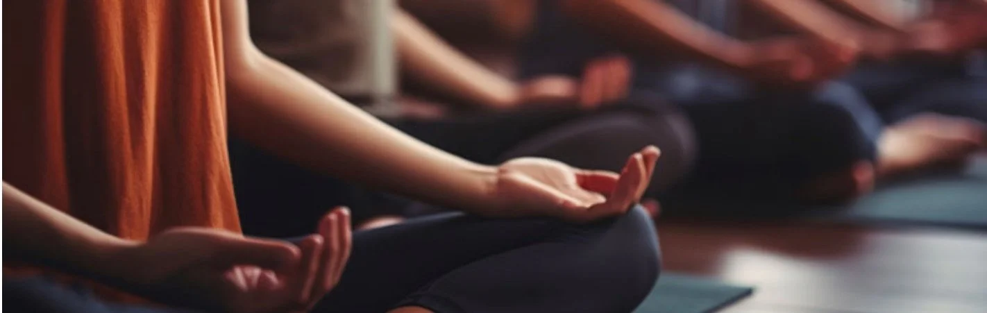 Persone in posizione di meditazione, sedute su tappetini, con le mani appoggiate sulle ginocchia in un ambiente calmo.