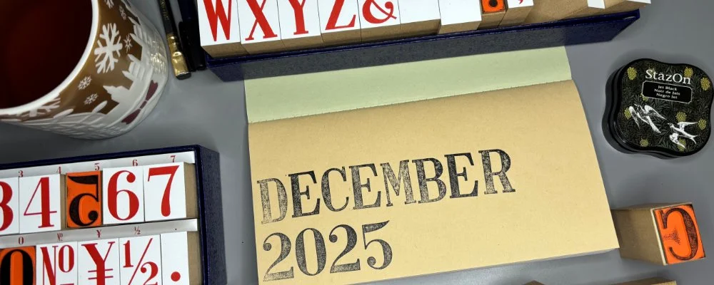 An open journal inset is stamped "DECEMBER 2025", surrounded by letter and number stamps, an inked and a cup of Earl Grey.