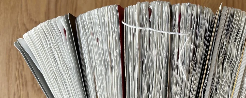 A pile of journals on top of a wooden surface, viewed from above so you can see the crinkled pages.