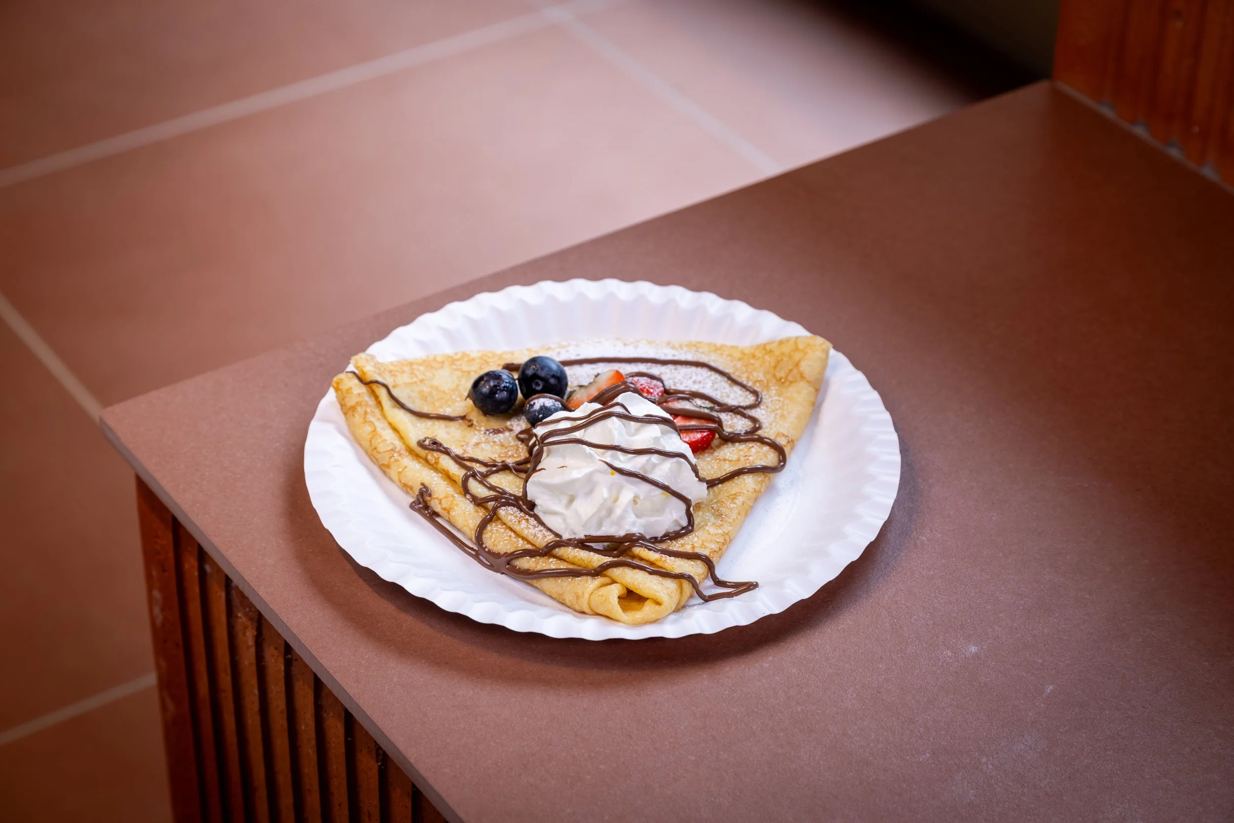 En serveringsfat med en stor amerikansk pannekake fylt med vaniljeis, toppet med blåbær, jordbær, sjokoladesirup og krem.