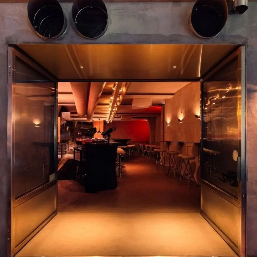 Open doorway of a modern restaurant and cocktail bar with warm ambient lighting, central bar counter, and minimalist seating arrangement in the centerof Lisbon