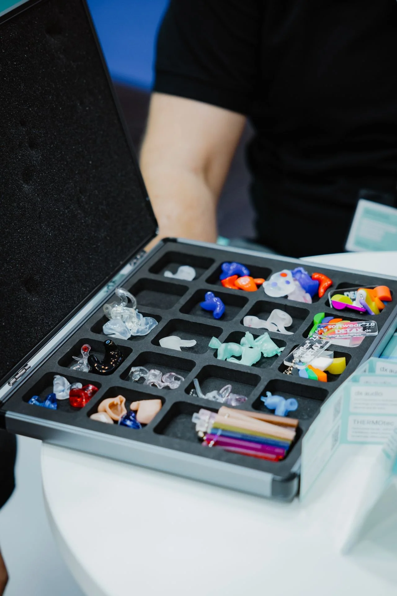 eine Aufbewahrungsbox mit bunten Gehörschutzstöpseln, Brillen und kleinen Gegenständen, die in einzelnen Fächern sortiert sind.