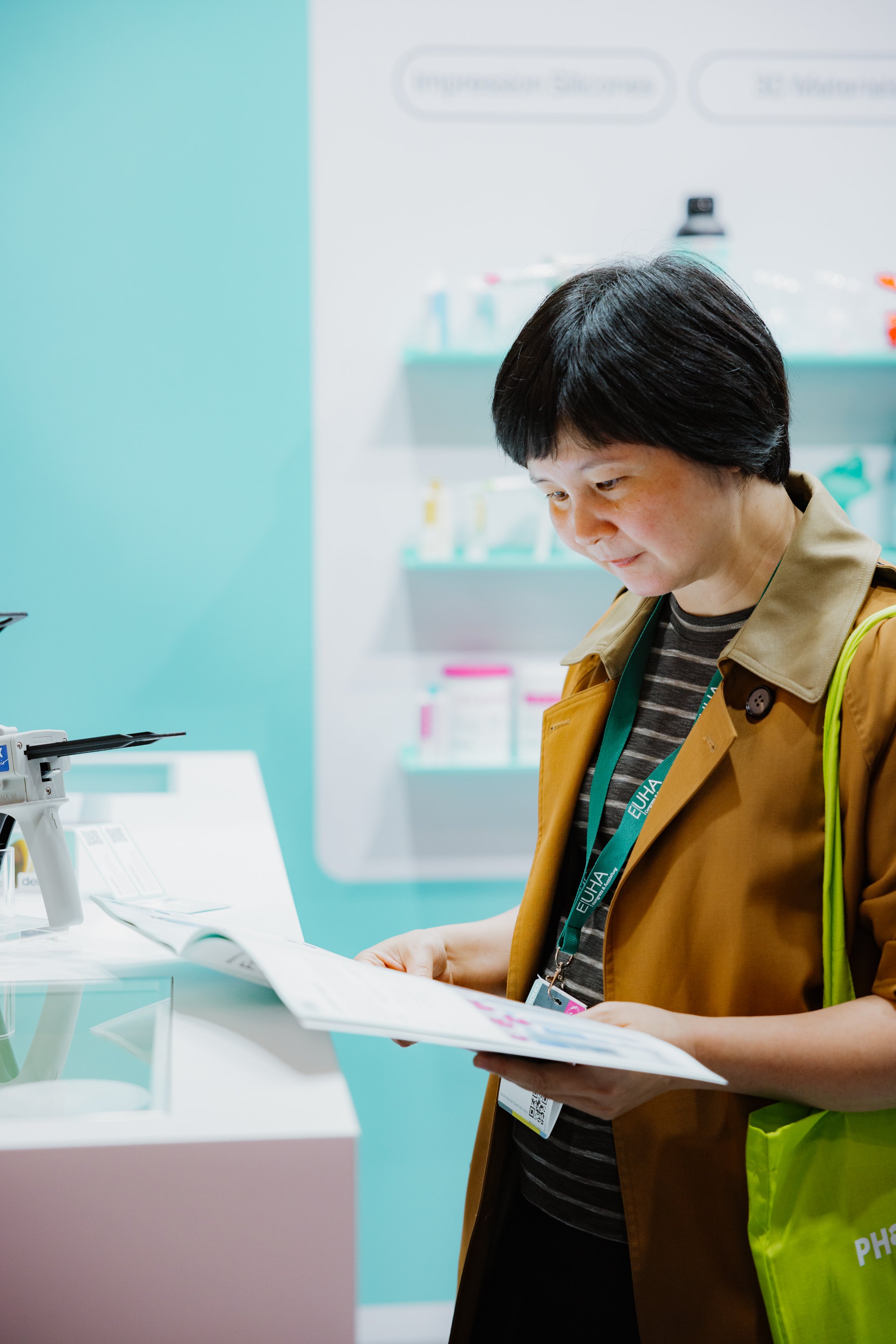 Frau mit schwarzem Kurzhaar, liest eine Broschüre, steht in einer Ausstellungshalle mit Medikamentenregalen im Hintergrund.