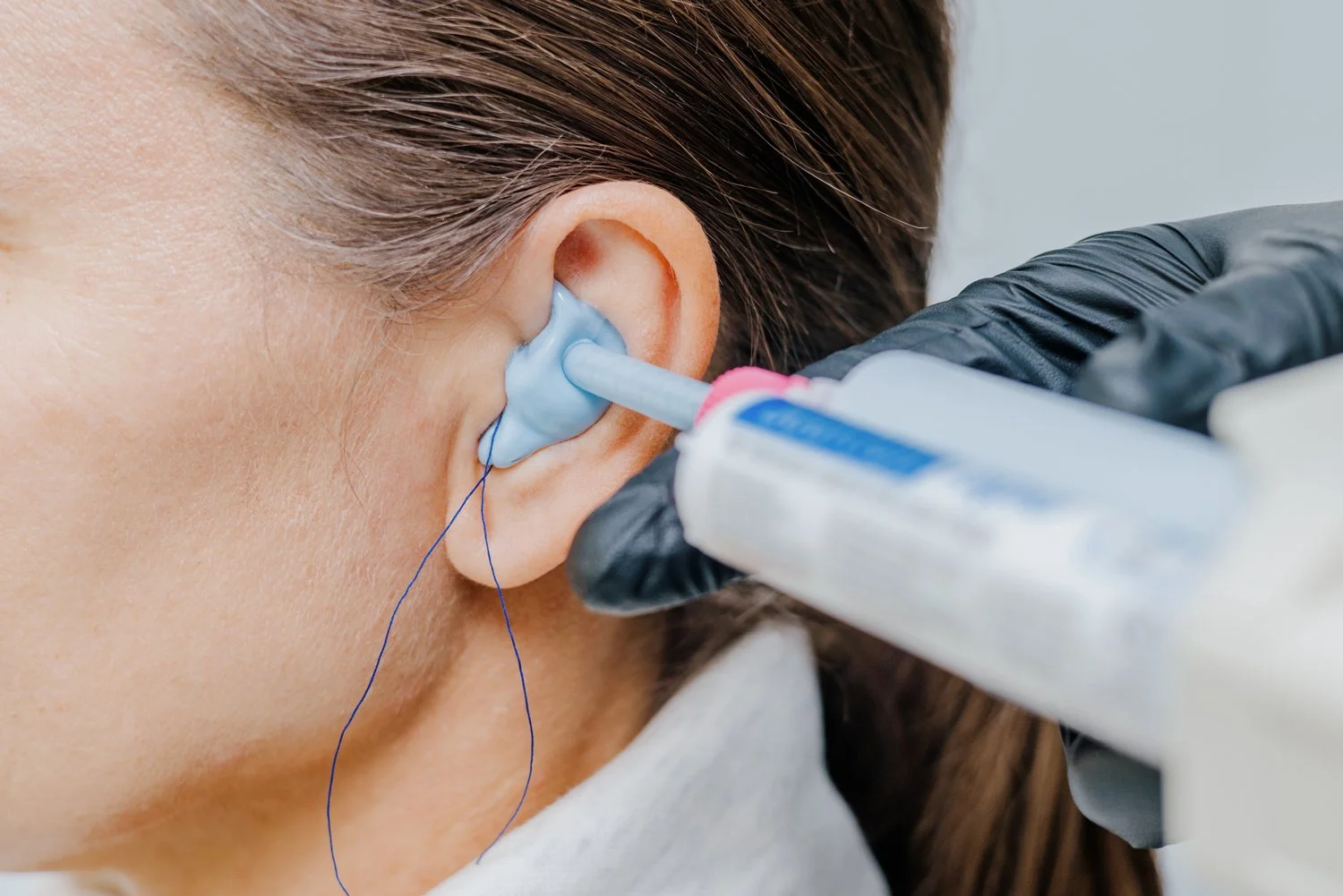Ärztliche Behandlung eines Ohres, bei der eine Flüssigkeit oder Arzneimittel mit einer Spritze in den Gehörgang injiziert wird. Der Arzt trägt schwarze Handschuhe und die Ohrregion ist sichtbar.
