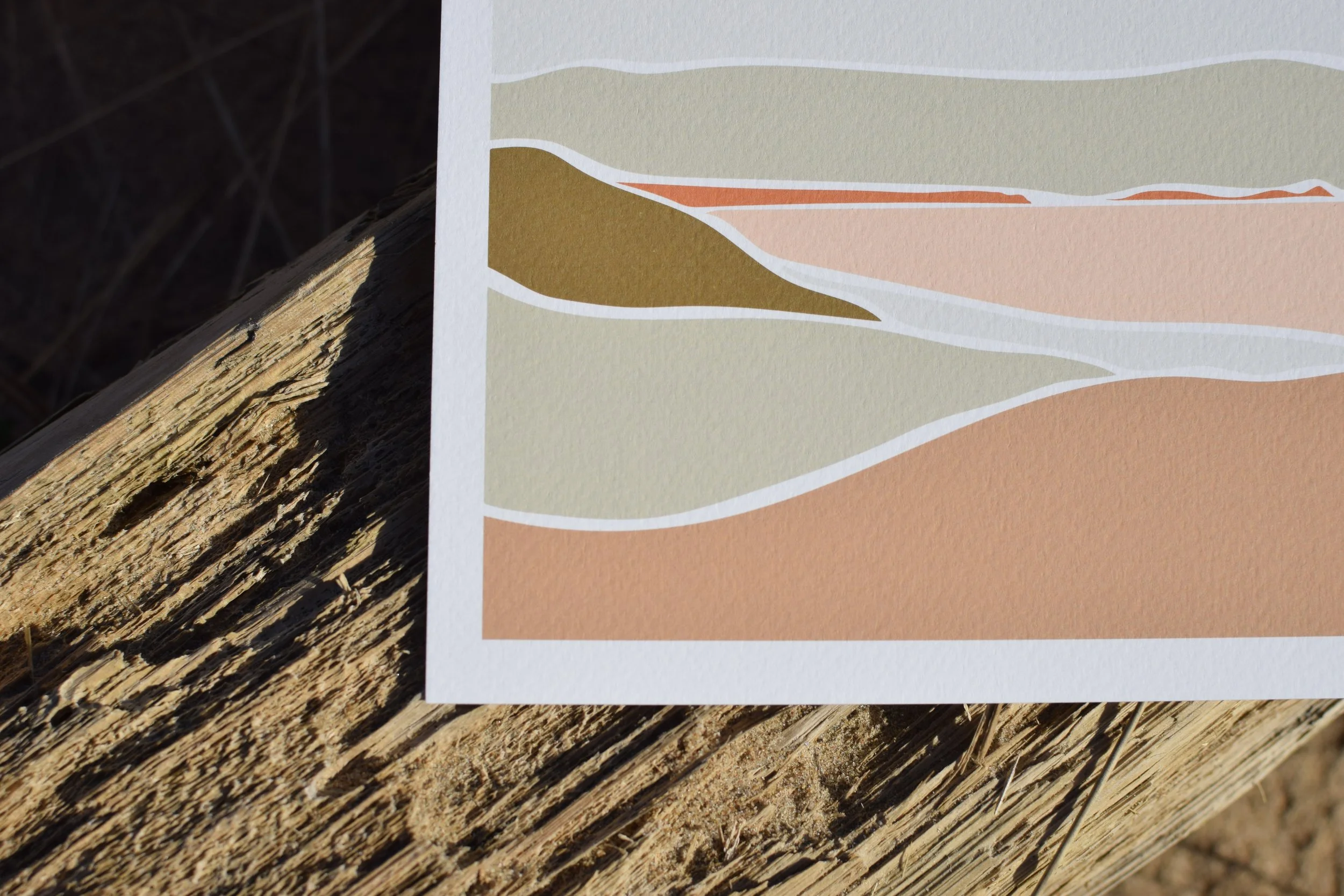 Colorful geological cross-section map showing different rock layers with white borders, laid on a textured wooden surface outdoors.