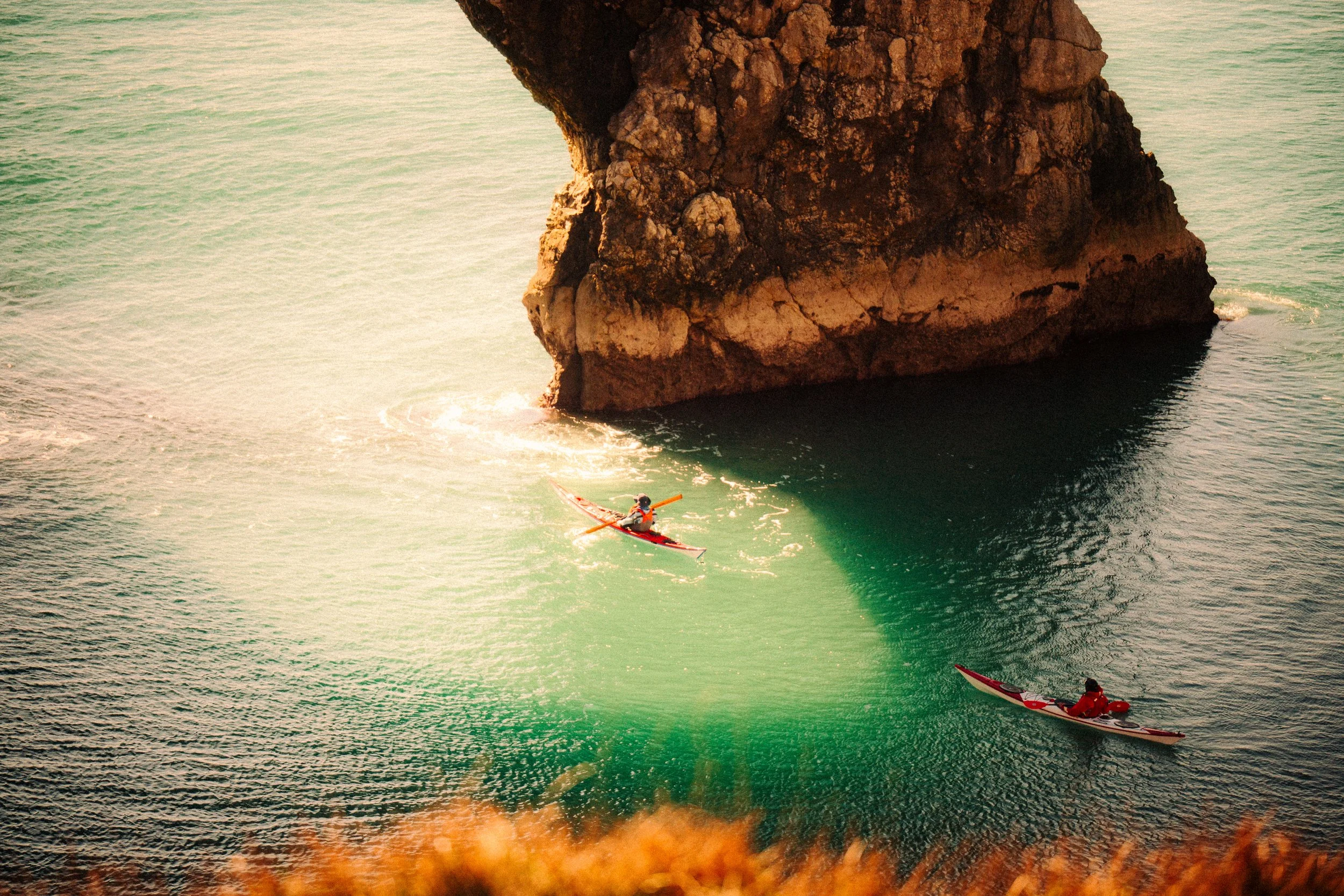 Two people kayaking near a large rock formation in the water during daylight.