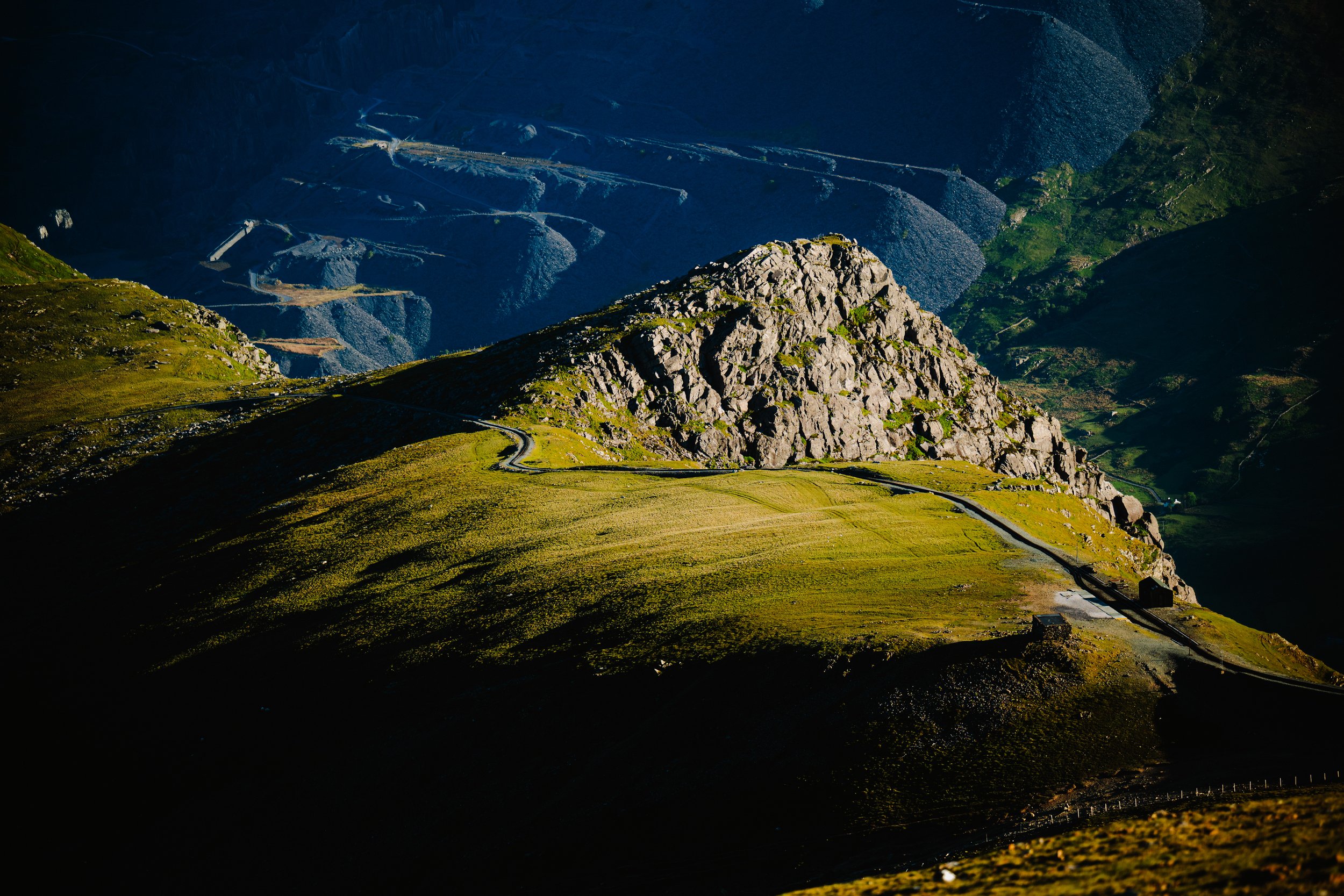 Mountain landscape with winding road and rocky hill, green fields and shadows in the valleys.