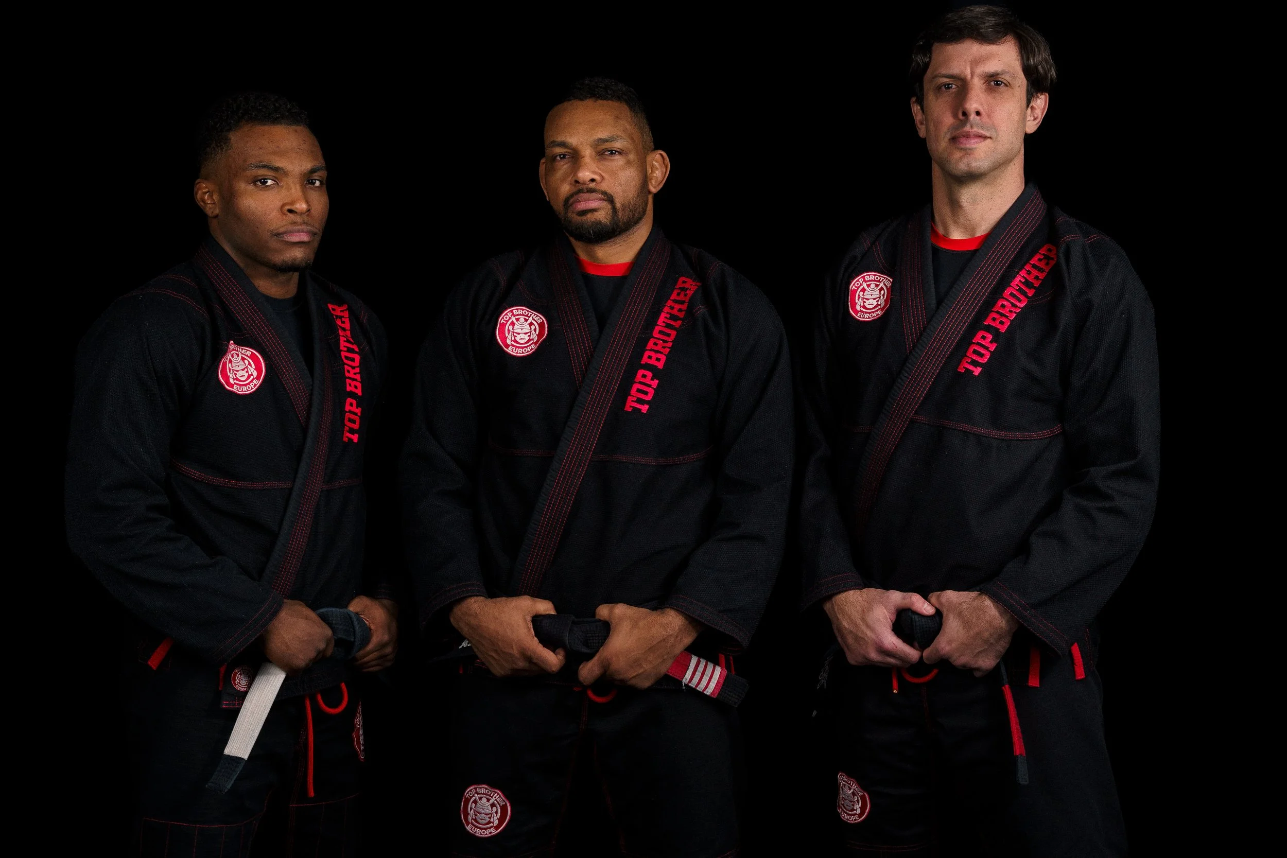 Studio portrait of the tree teachers from Top Brother Düsseldorf, Alex Malheiro, Renan Malheiro e João Macedo, wearing black gis, looking straight at the camera.