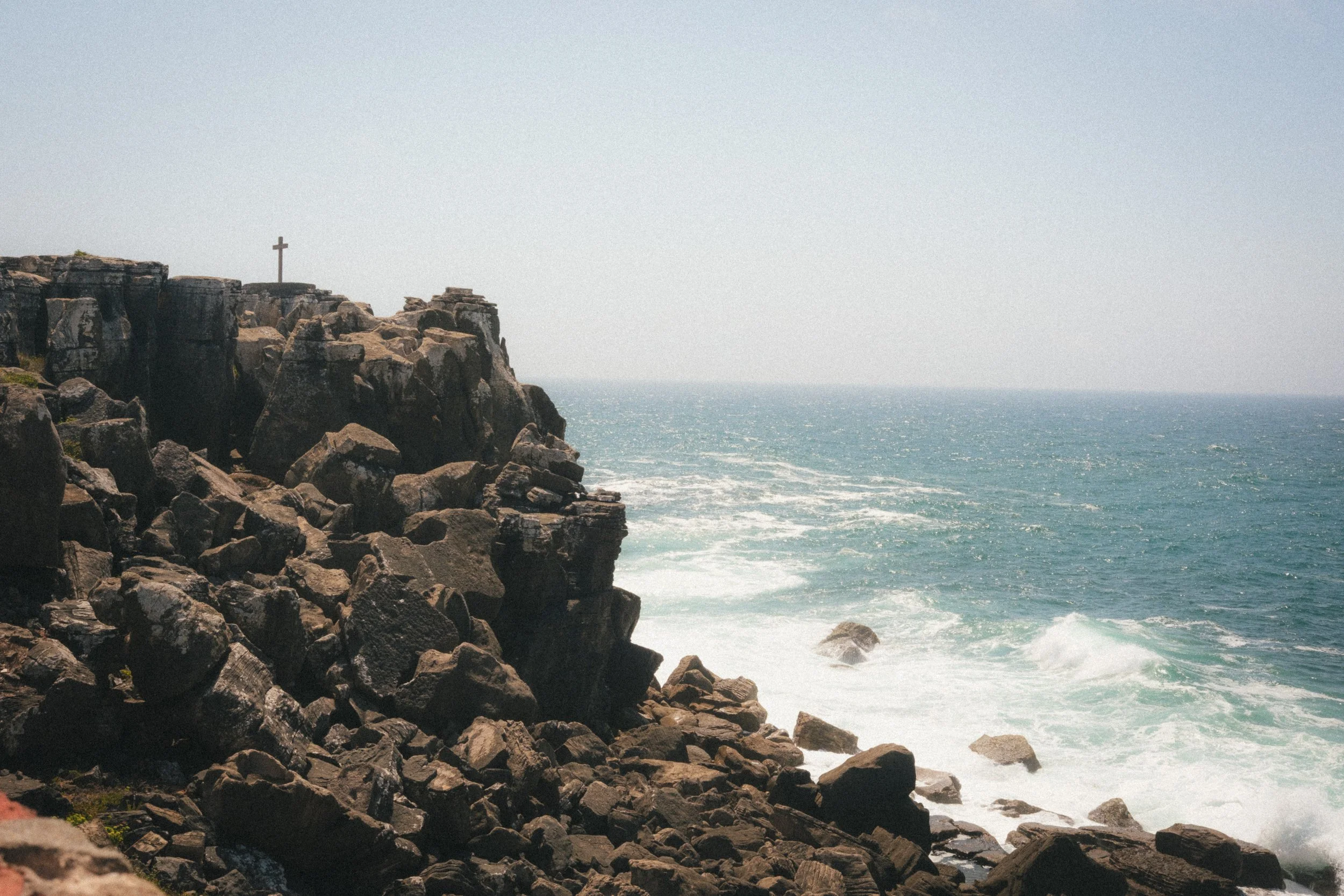 Fine art travel photography of the Atlantic coastline in Peniche, Portugal, featuring dramatic rocky cliffs and crashing ocean waves under a clear sky.