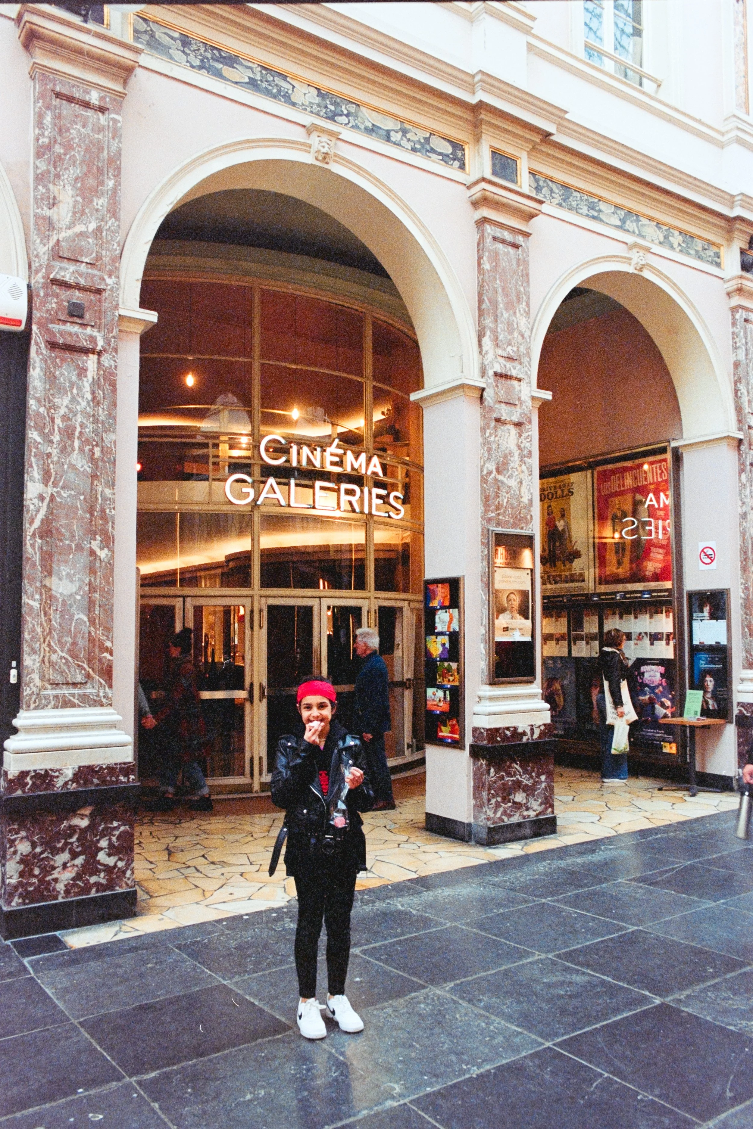 Fine art travel photography featuring Maria Alice Costa standing in front of Cinéma Galeries in the Galeries Royales Saint-Hubert, Brussels. Capturing the charm of historic European architecture with personal and cultural elements, perfect for art co
