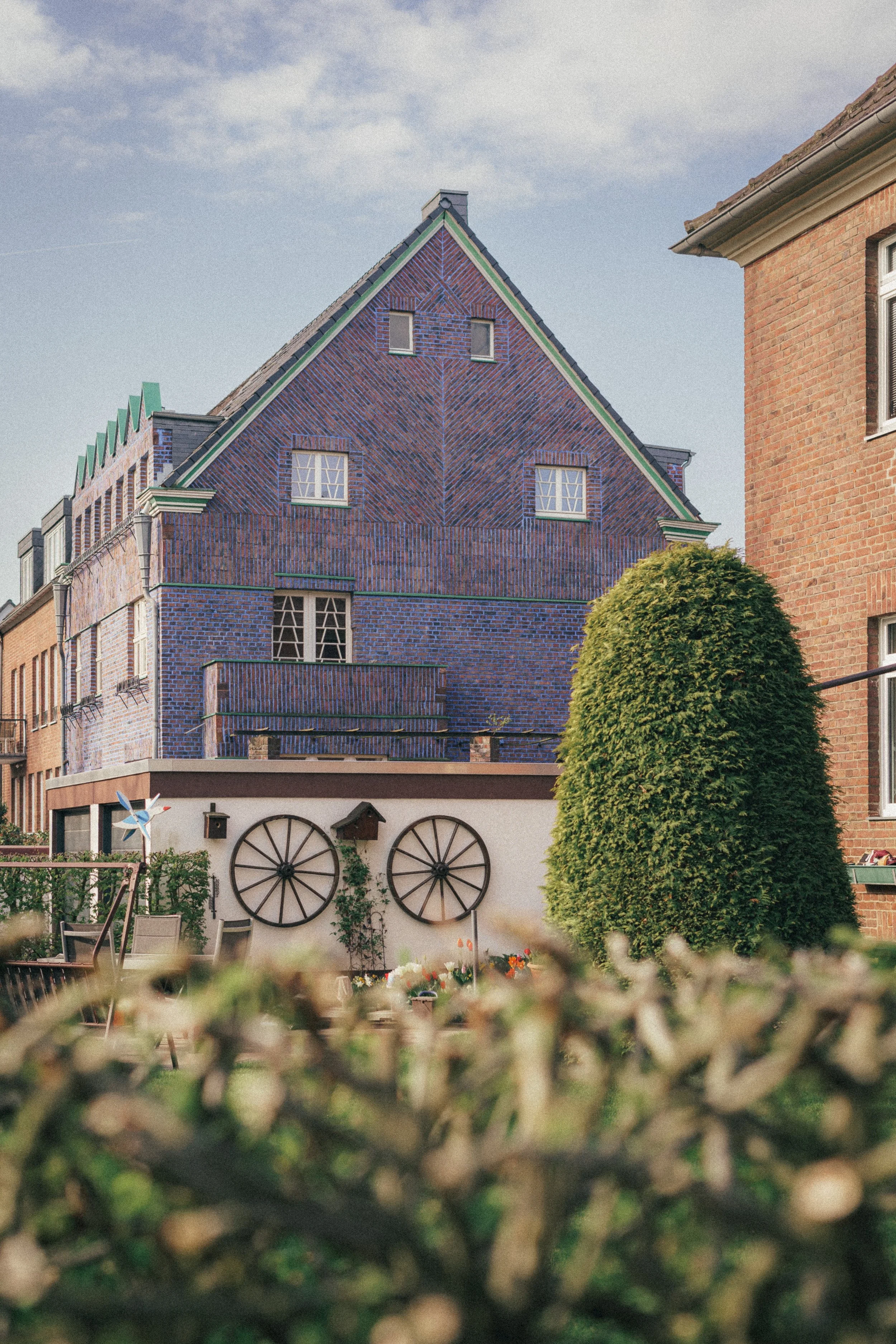 Fine art photography of a blue/violet building featuring two wheels that look like eyes and a tree that looks like a nose, making the house look funny like a cartoon. The blue sky stand in the background.