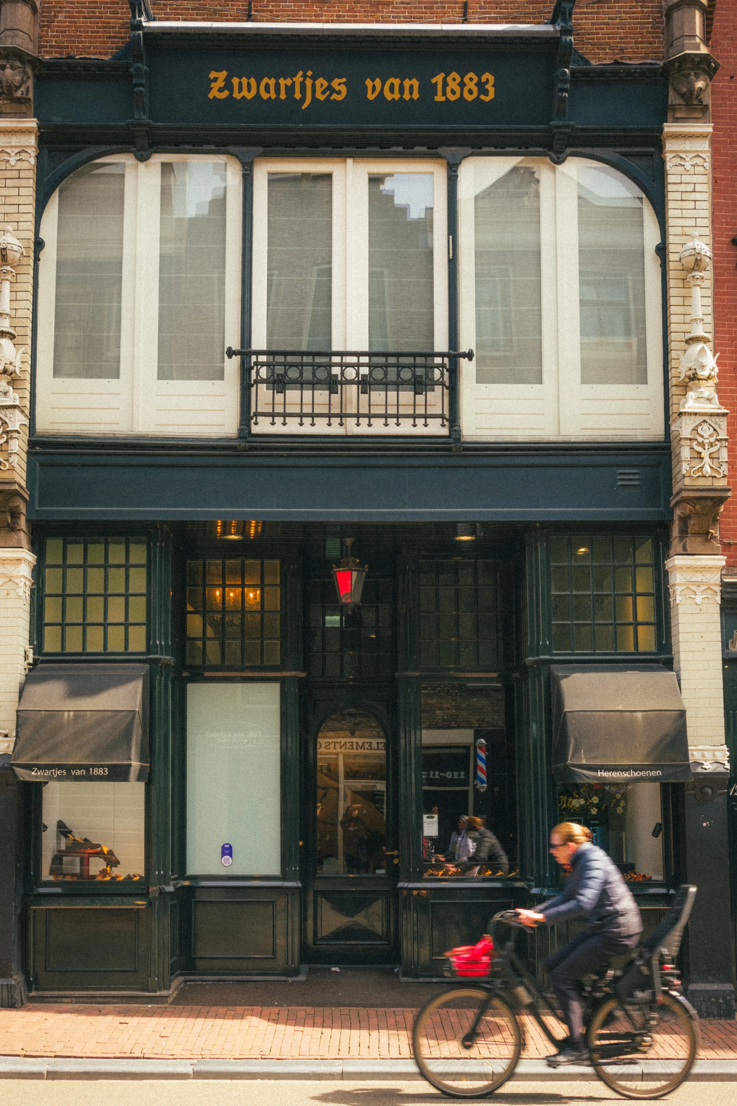 "Fine art photo of Zwartjes van 1883, an iconic storefront in Amsterdam, capturing historical Dutch architecture and a cyclist in motion, perfect for collectors of urban and cultural imagery.
