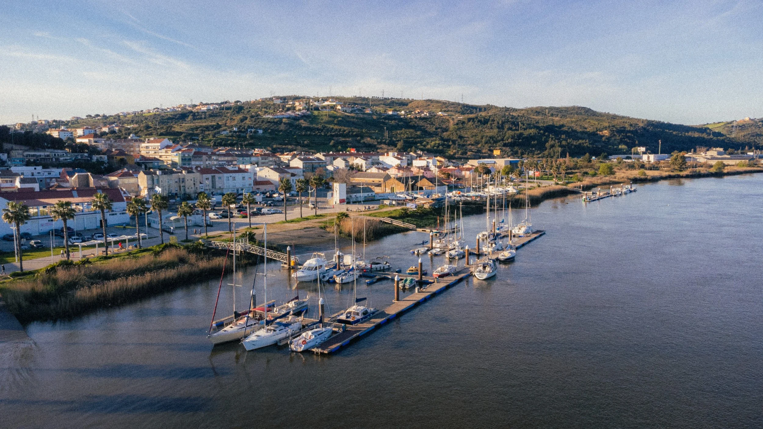 Fine art landscape of the docks in Alhandra, Portugal. In the middle are the boats in the docks the water in the foreground followed by the city and the blue sky.