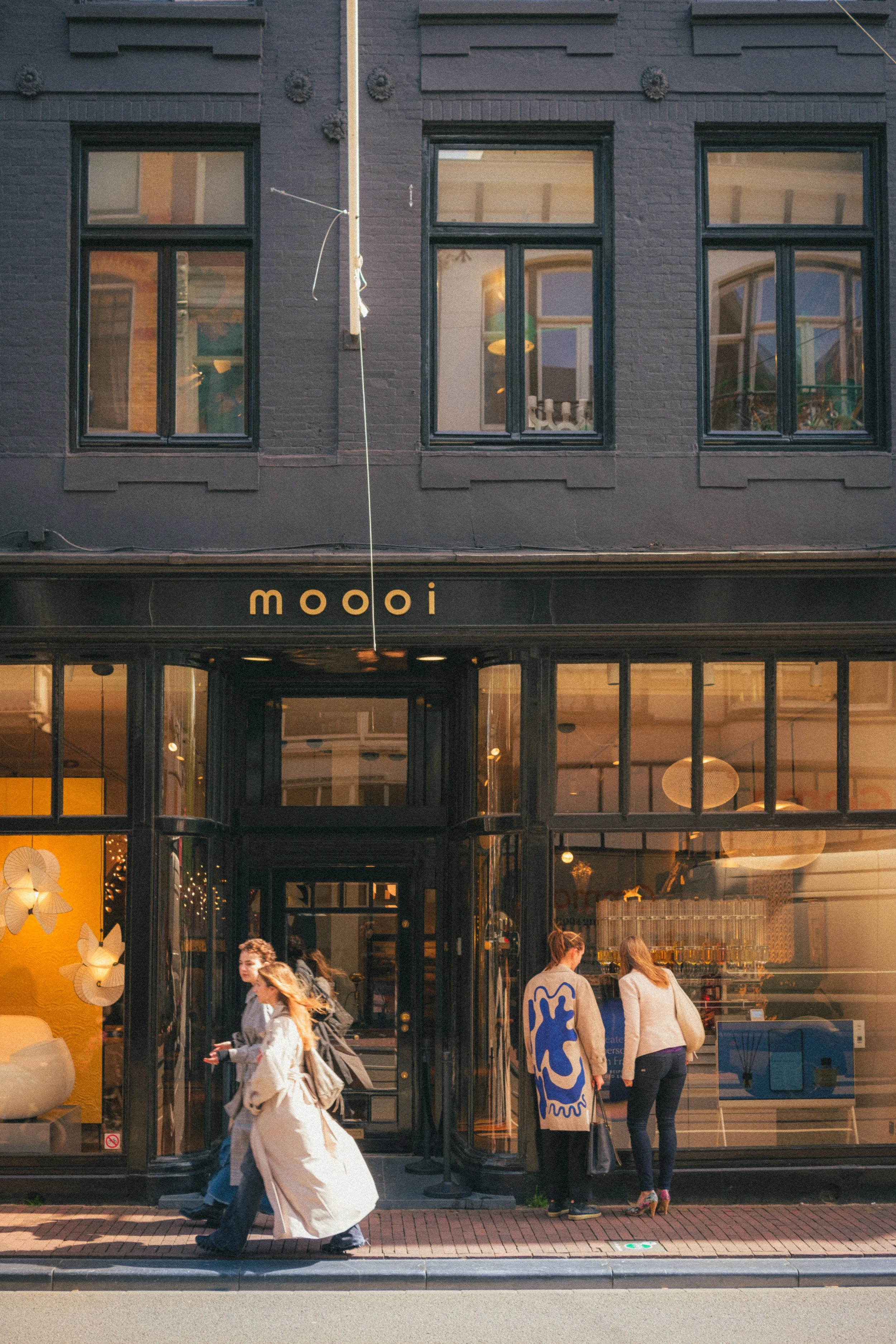 Street view of the Moooi design store in Amsterdam, showcasing contemporary architecture, vibrant storefront displays, and pedestrians in motion. A fine art urban photograph capturing the essence of Amsterdam's design and lifestyle for an exclusive p