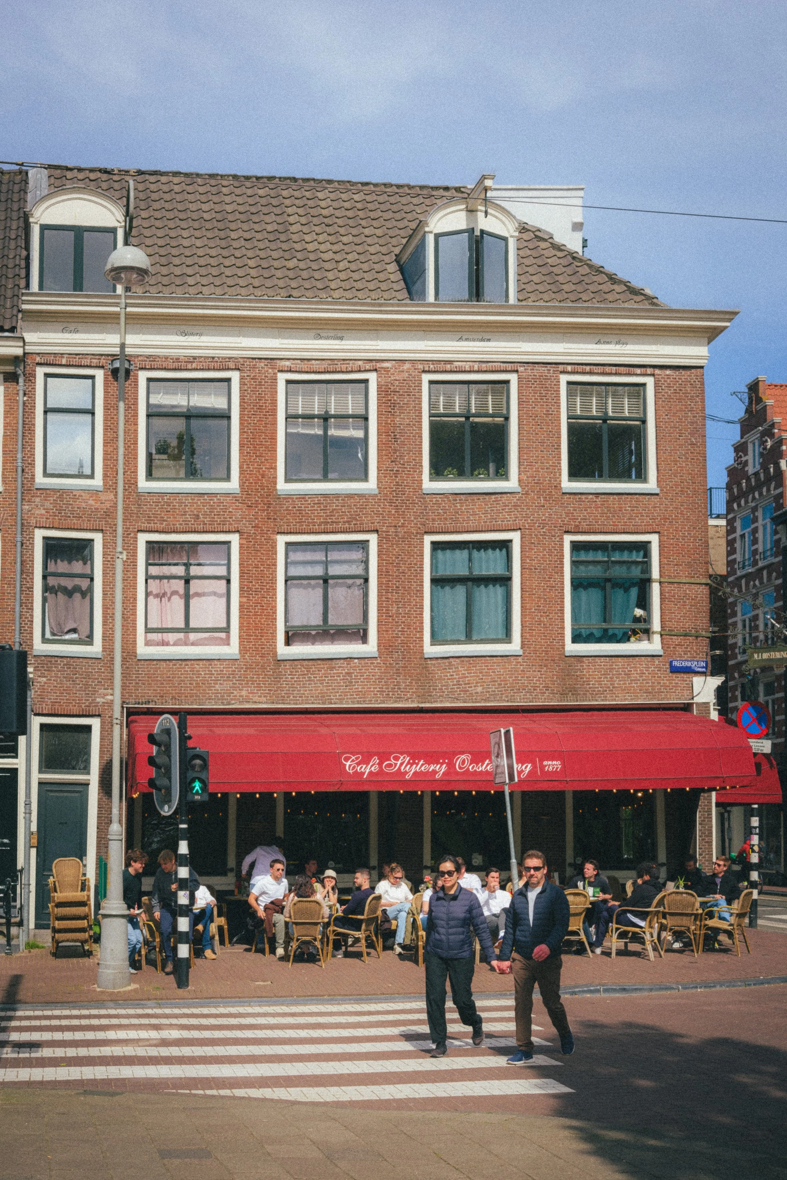 Street view of Café Slijterij Oosterling in Amsterdam, highlighting its charming architecture, red awning, and lively outdoor seating. Captured as part of a fine art urban photography series in the Netherlands.