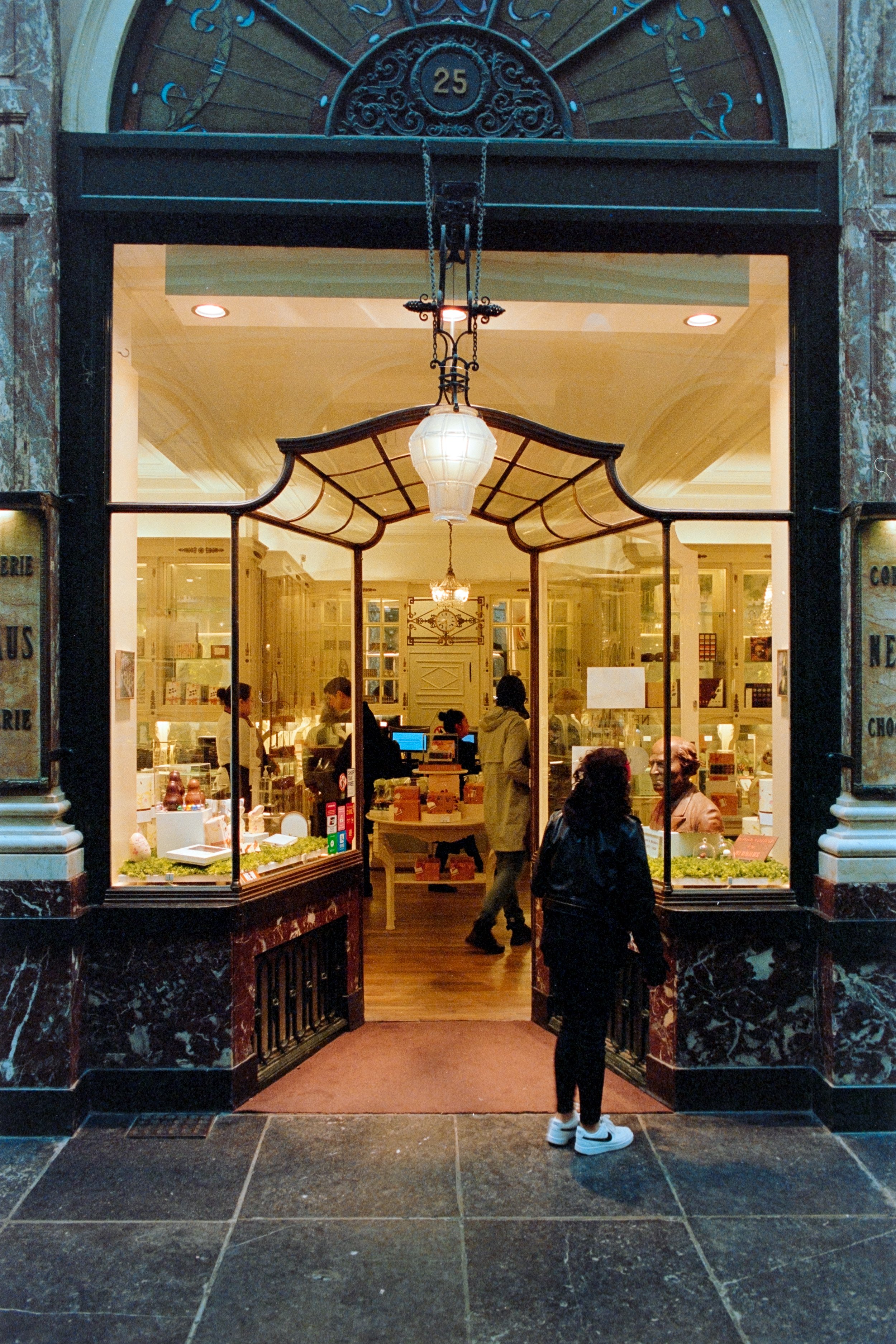 Elegant storefront in the Galeries Royales Saint-Hubert in Brussels, Belgium, featuring intricate architecture, a vintage hanging lantern, and a display of fine chocolates and confections inside the boutique.