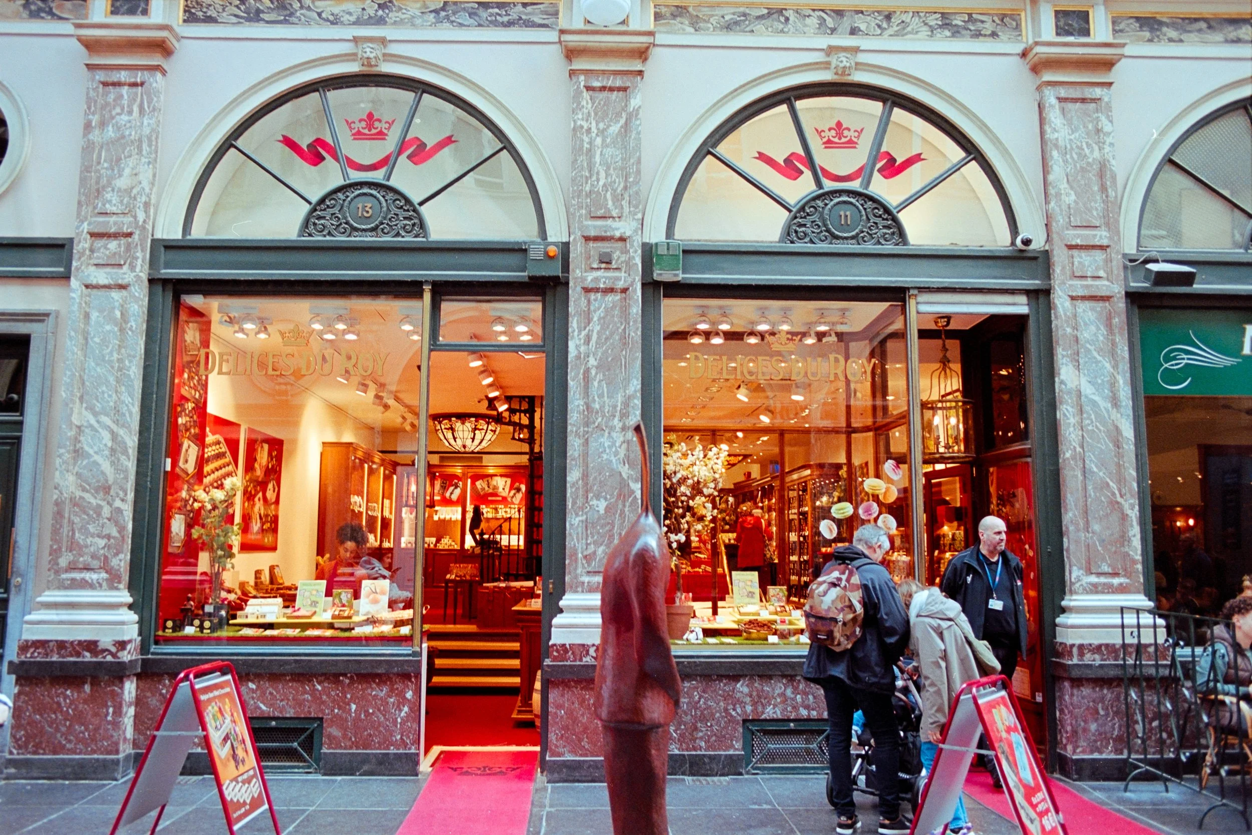 Exclusive fine art travel photography of the elegant Délices du Roy chocolate shop inside Galeries Royales Saint-Hubert, Brussels, Belgium. Captures the luxurious charm of the historic shopping arcade with vibrant red decor and architectural elegance