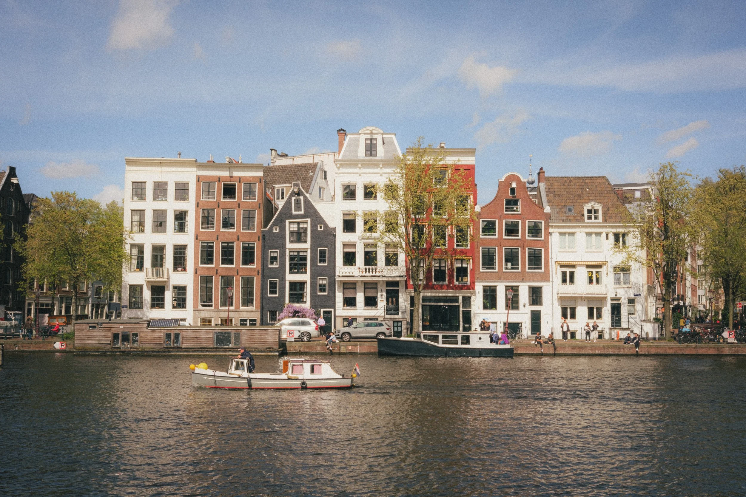 Fine art landscape of the crooked houses in Amsterdam, Netherlands. On the front stand two boats on the river and on the back the unaligned building and the sky.