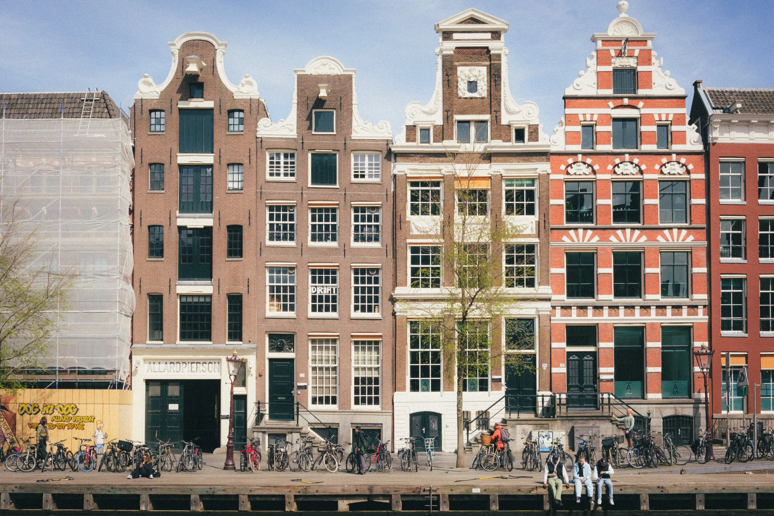Fine art photograph capturing iconic Dutch canal houses in Amsterdam, showcasing classic gable architecture, vibrant urban life with bicycles, and serene waterfront vibes, ideal for premium fine art prints and exclusive photography collections.