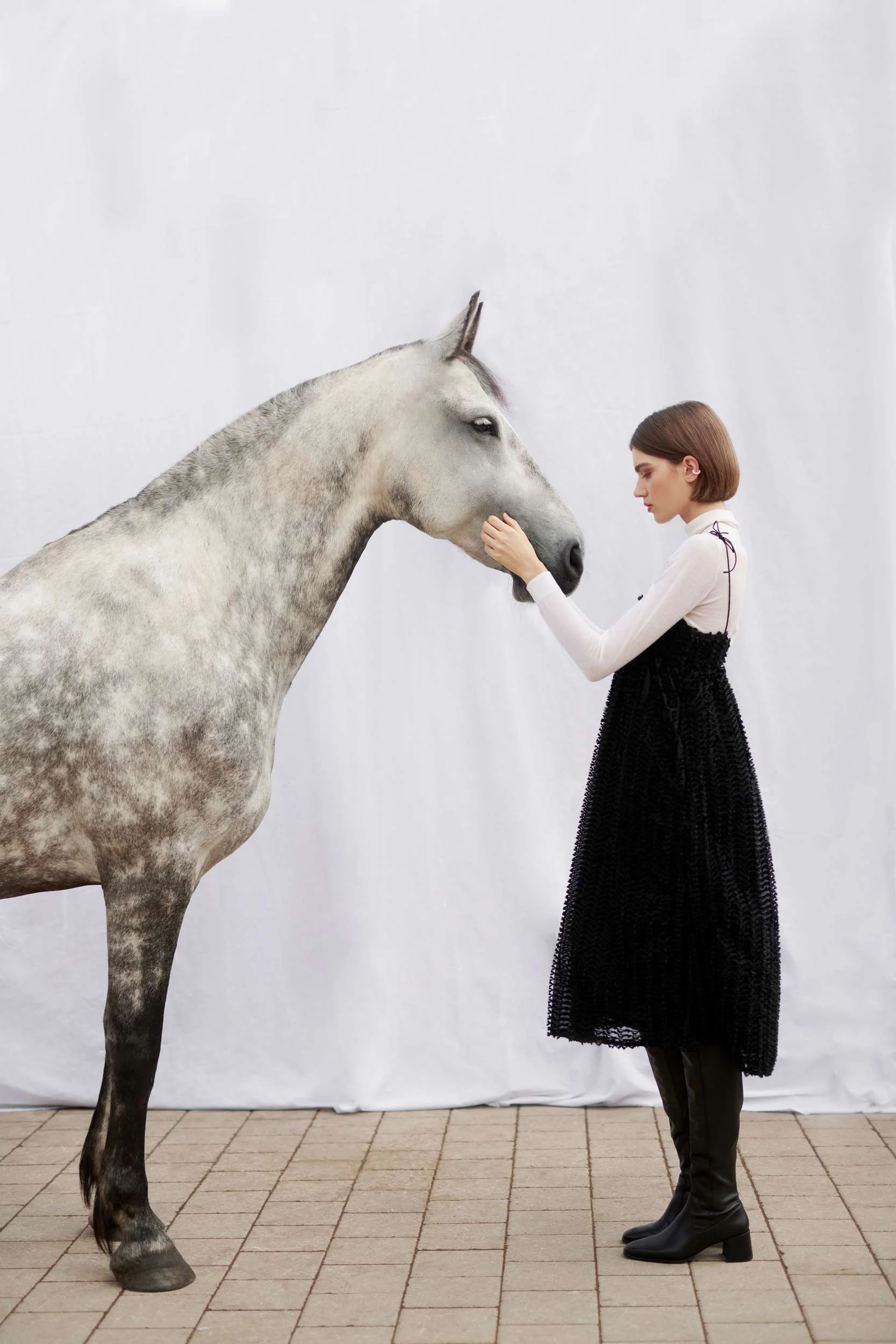 Model in a black skirt facing a grey horse in front of a white backdrop