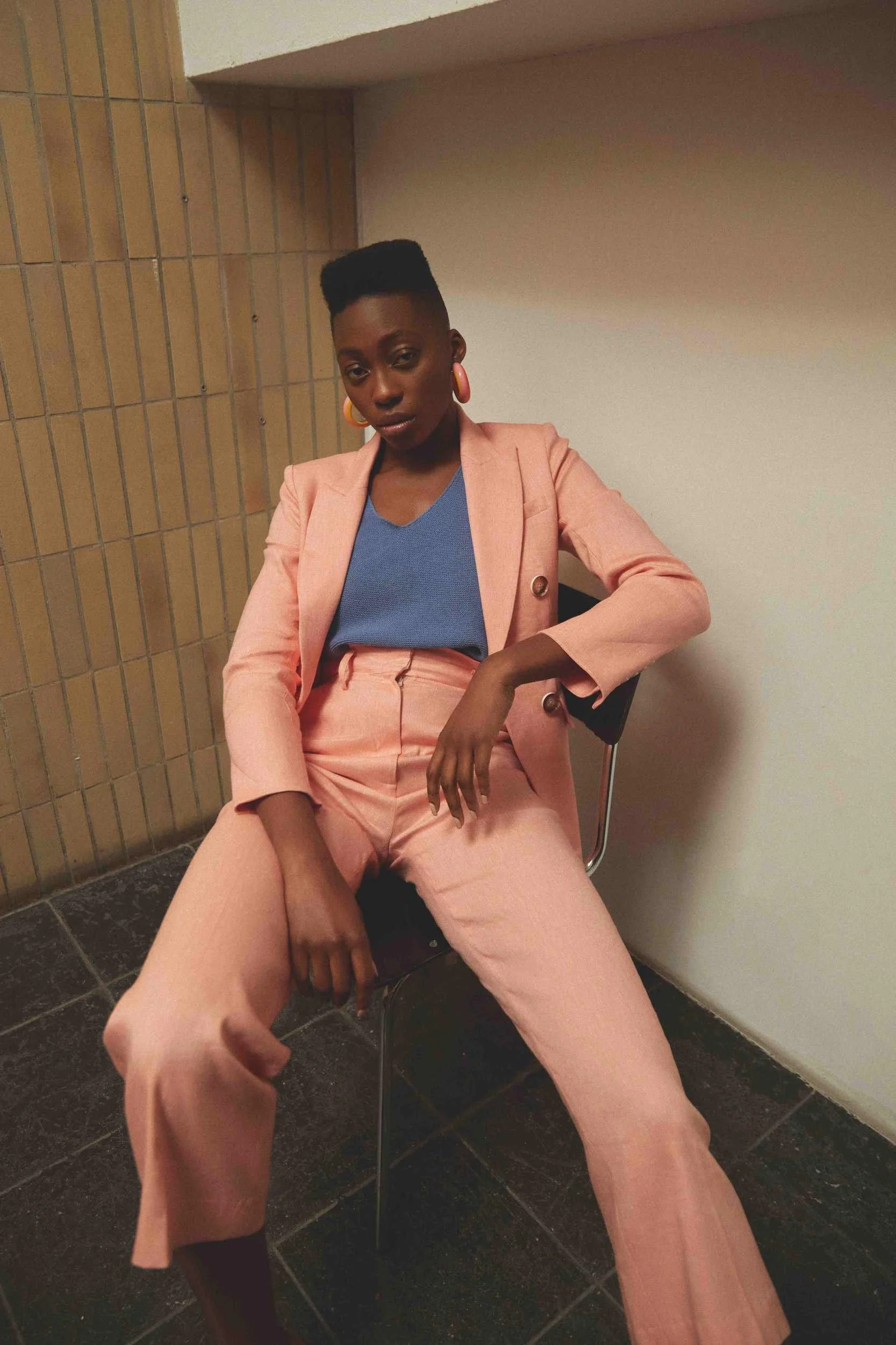Pink suit with a blue top, seated against a wall
