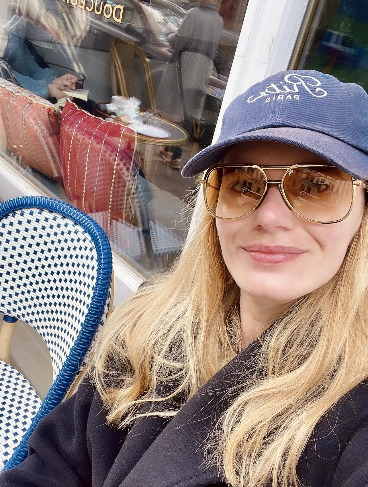 Portrait of fashion stylist Anita Bauer in a navy cap and tinted sunglasses outside a café