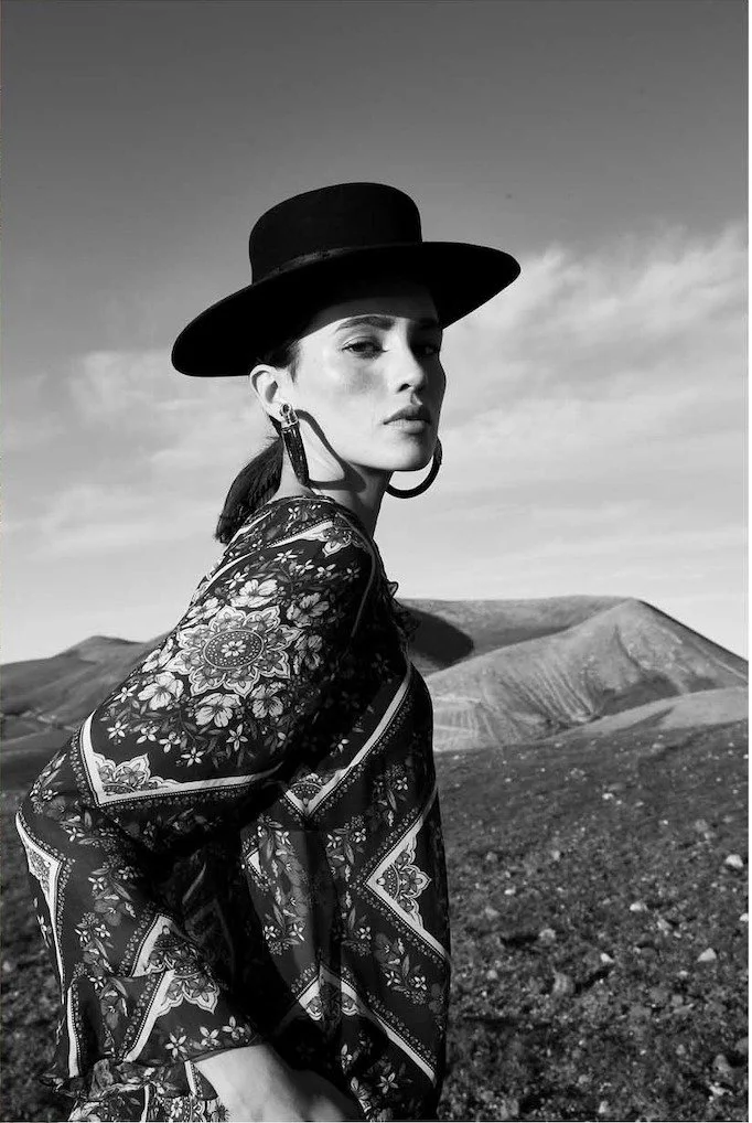 Wide brimmed hat and a printed jacket in a volcanic landscape, black and white, styling Anita Bauer