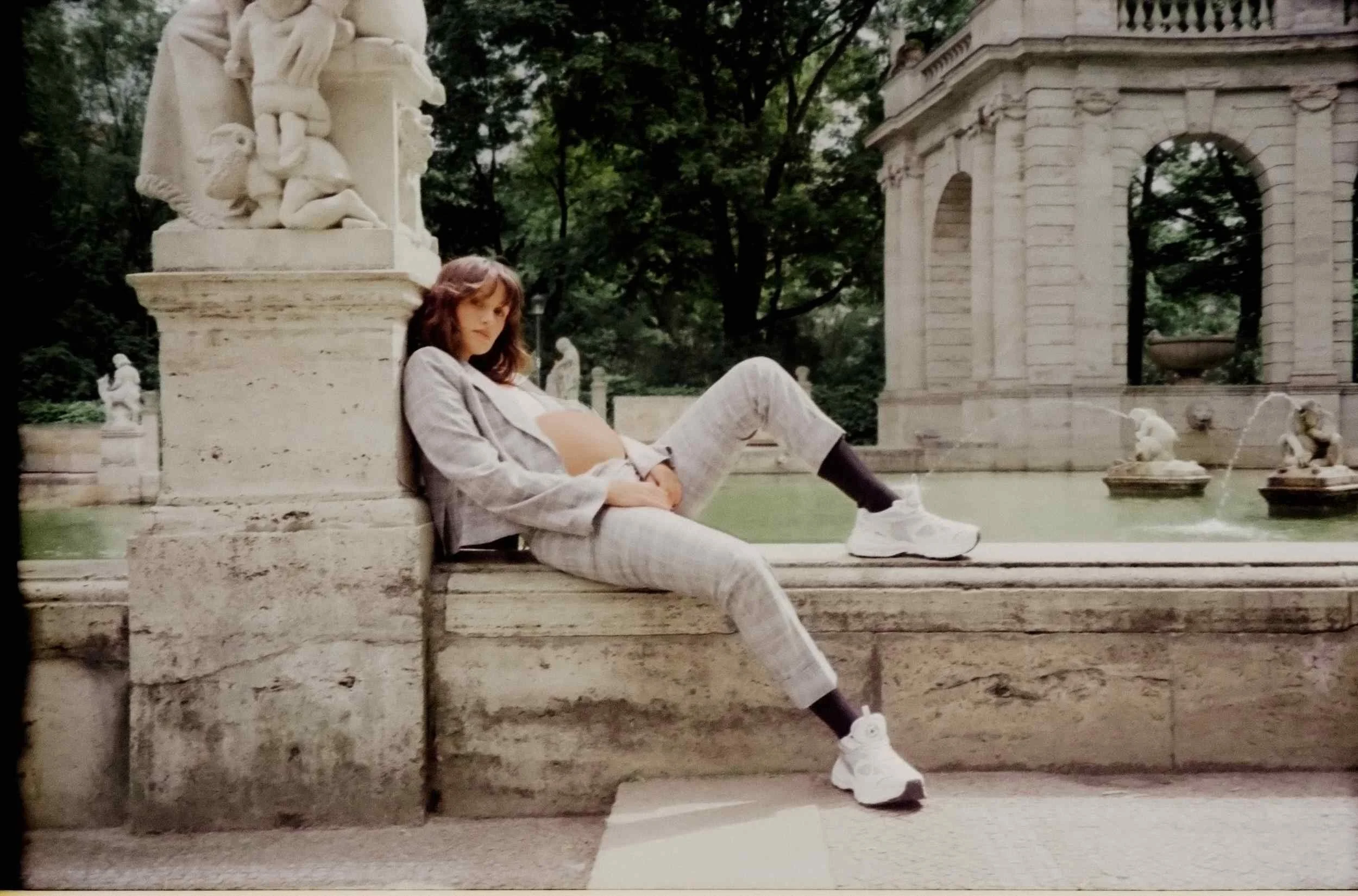 Mogli seated at a fountain in a white outfit and sneakers