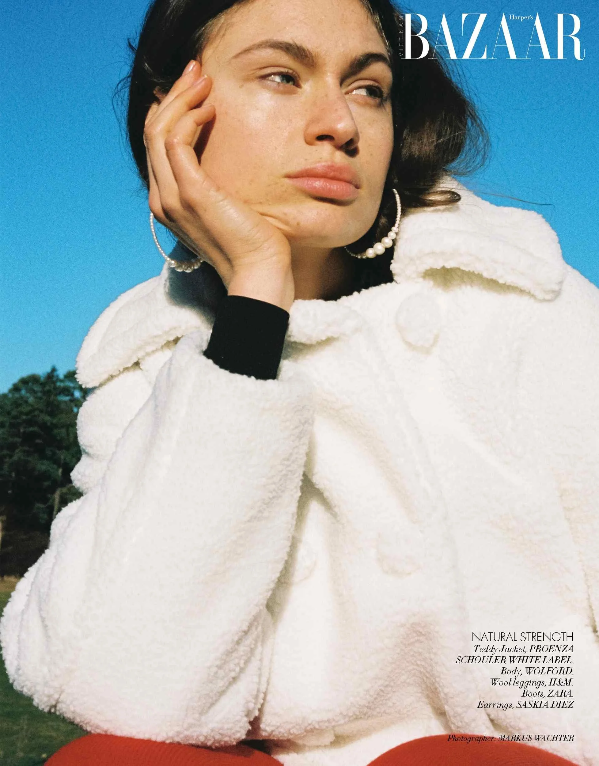 Harper's Bazaar Vietnam editorial: white teddy jacket, hand at the cheek, blue sky