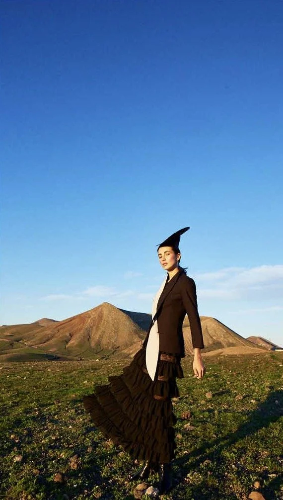 Black look with a hat in front of volcanic hills and a blue sky