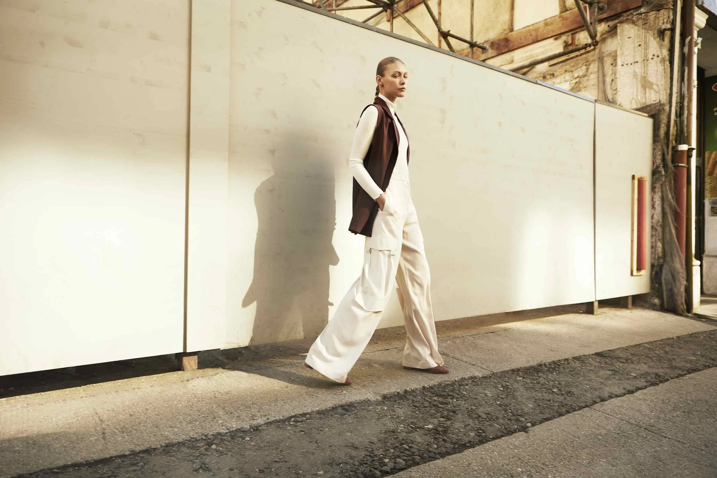 White trousers and a dark waistcoat walking along a white wall