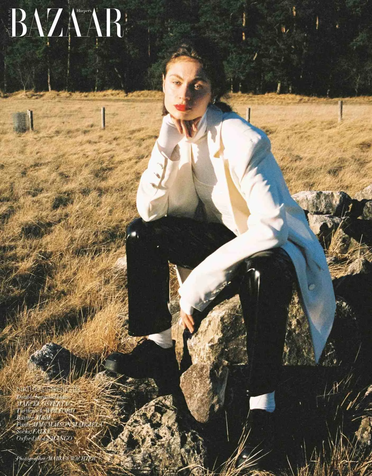 Harper's Bazaar Vietnam editorial: white blazer and black trousers, seated on a rock