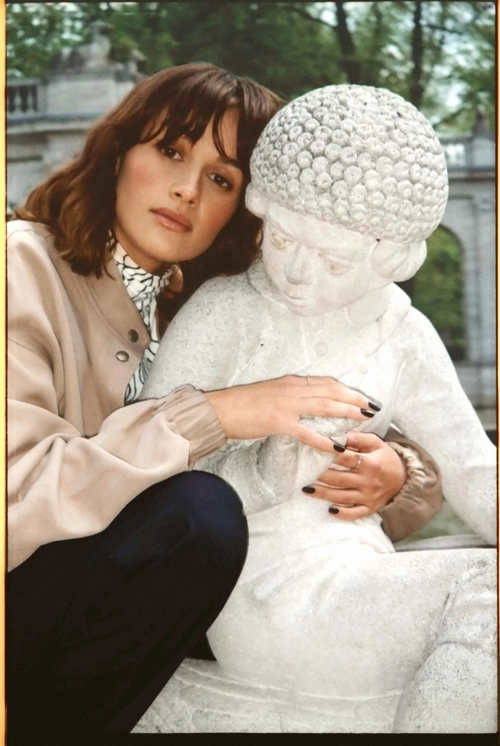 Mogli in a cream coat beside a stone statue