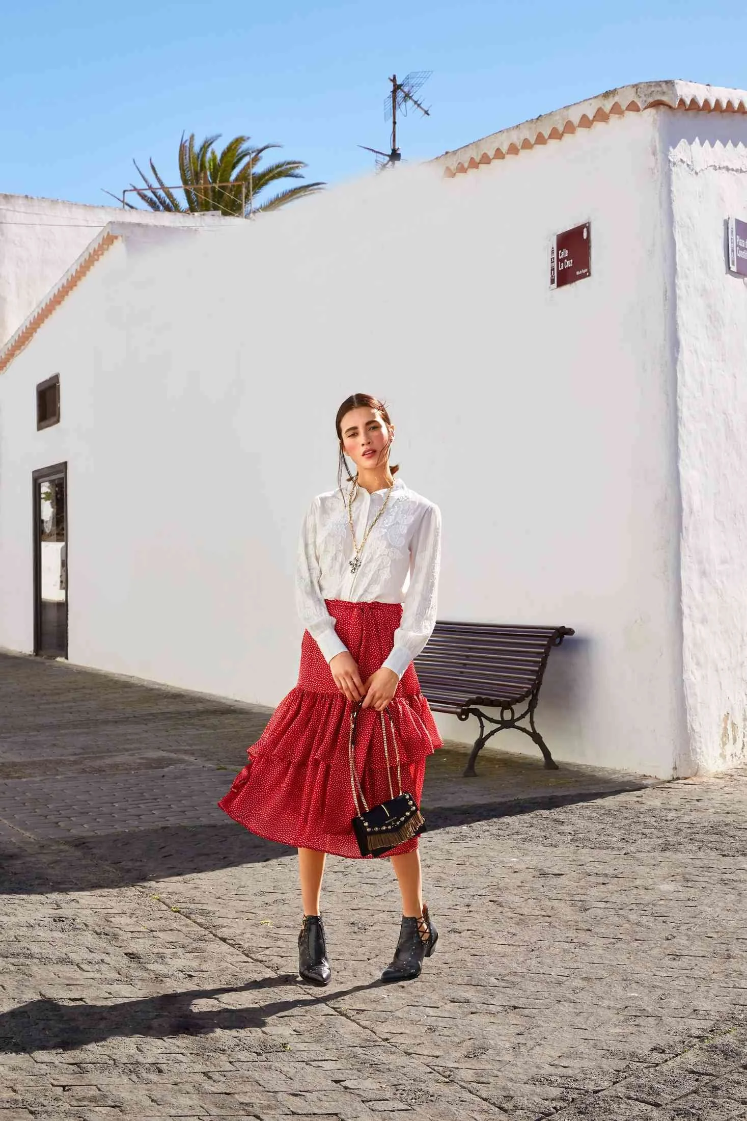 White blouse and red skirt in front of a white wall with a bench