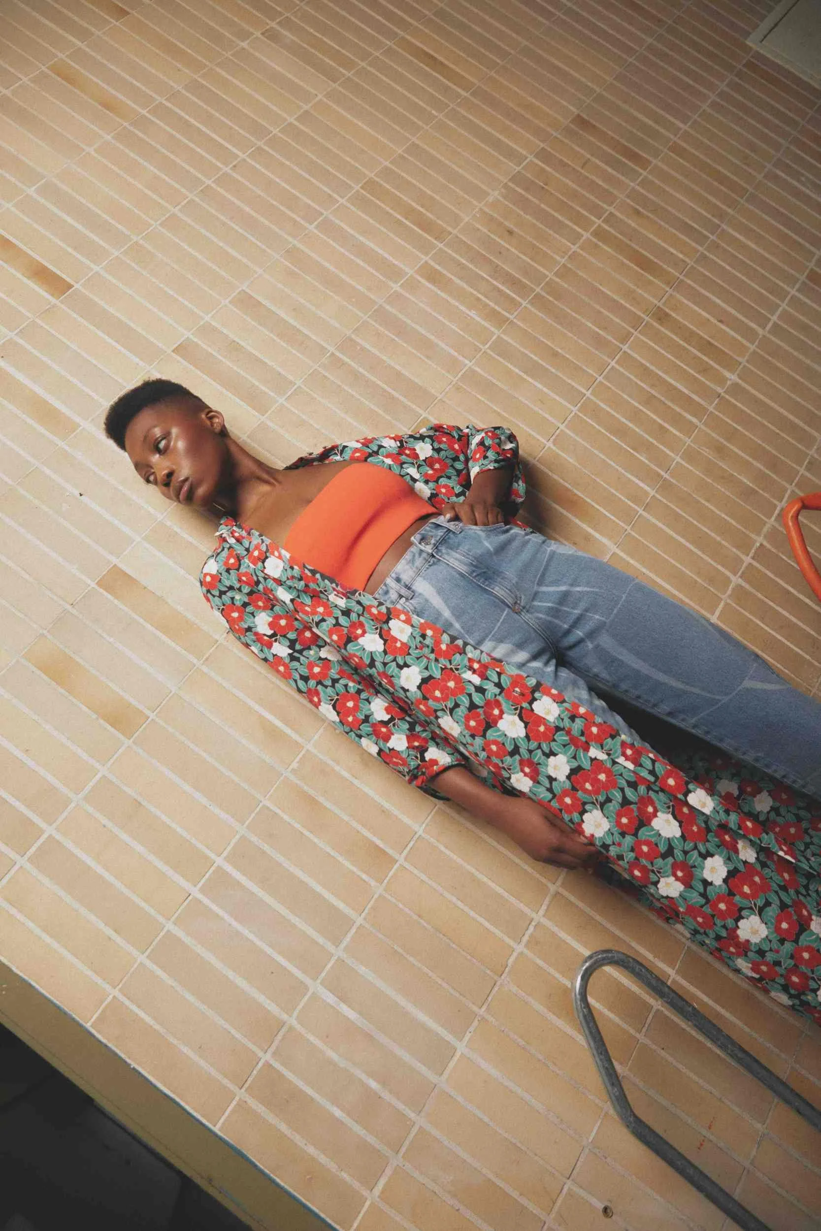 Model lying on tiles in floral trousers and an orange top, FOGS Magazine, styling Anita Bauer