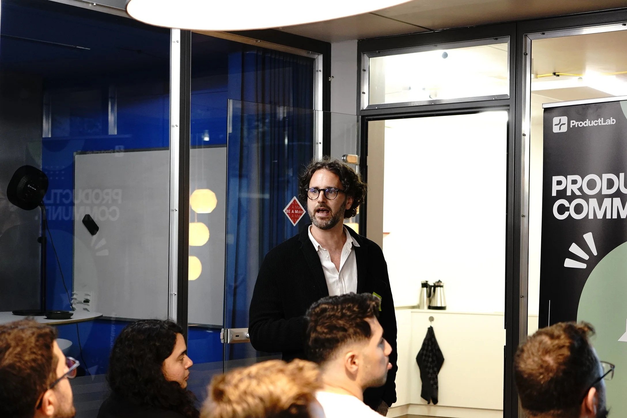 Alessio Tixi presenting in front of an audience at a ProductLab community event, with people seated and listening attentively.