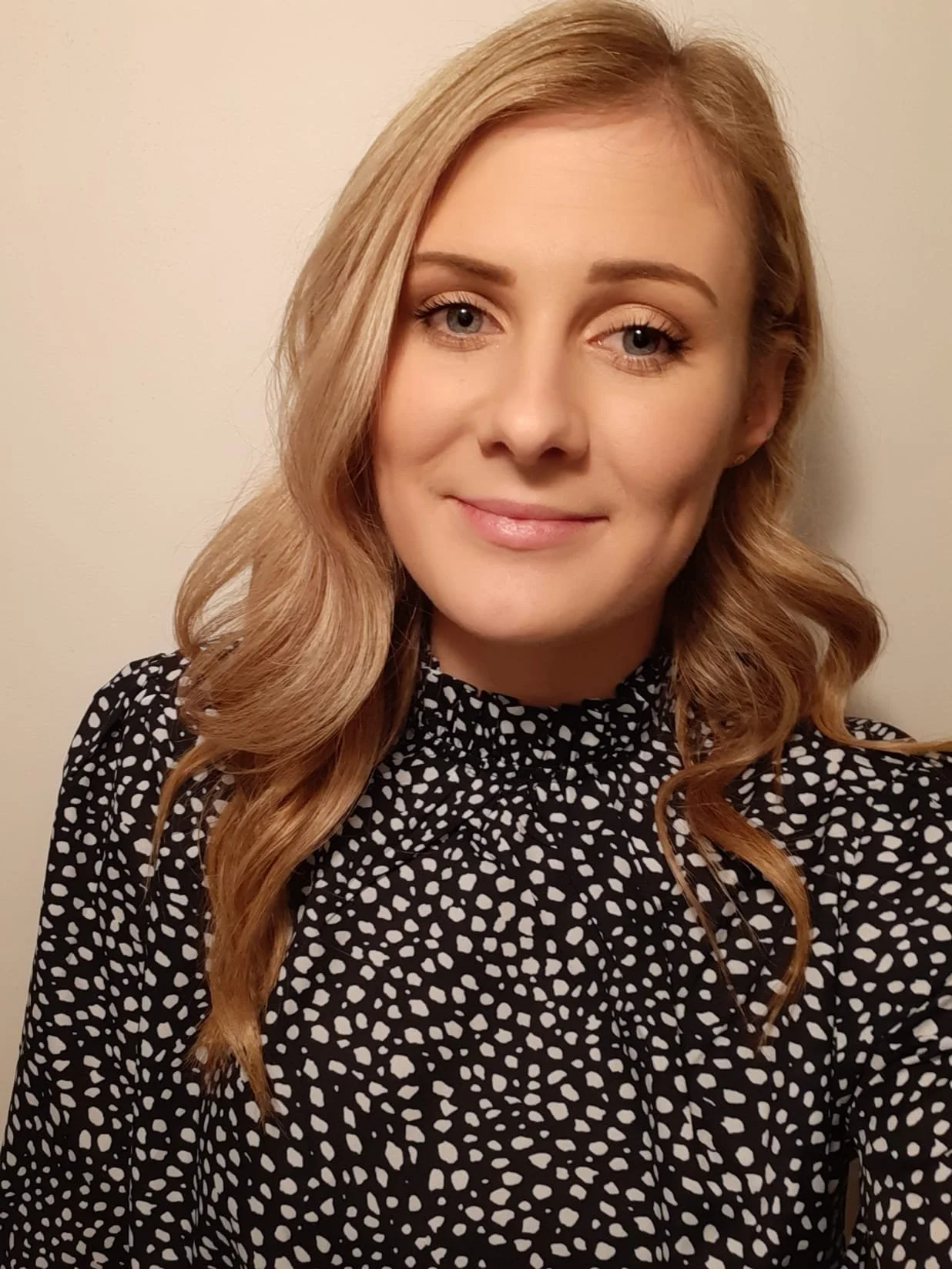 Portrait of Tabatha. Her blonde, medium length hair has a wave to it, and she wears a black and white polka dot, high necked blouse.