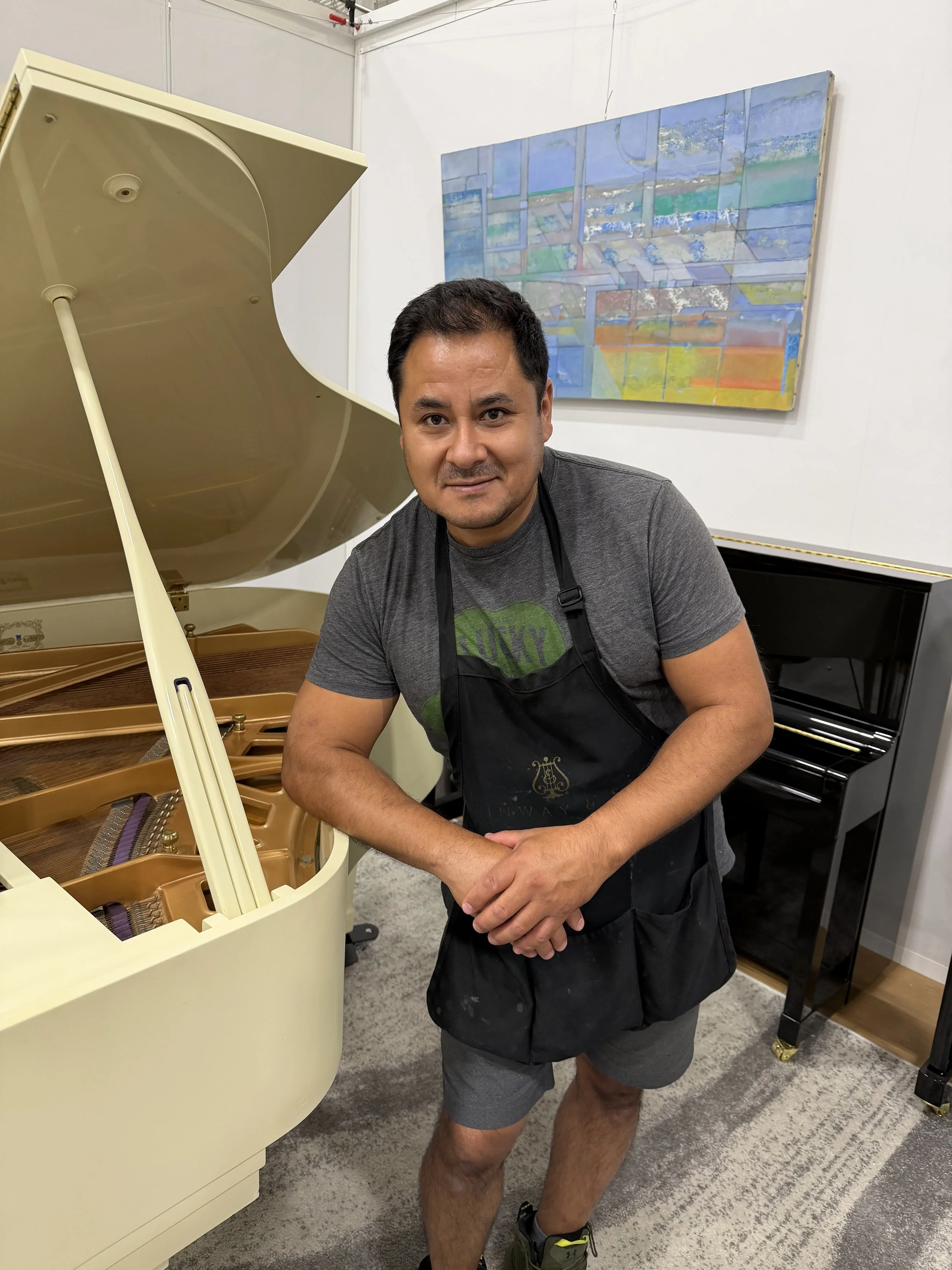 Edson Guevara piano finish repair specialist standing in front of a white lawyer Kawai grand piano in a piano store showroom.