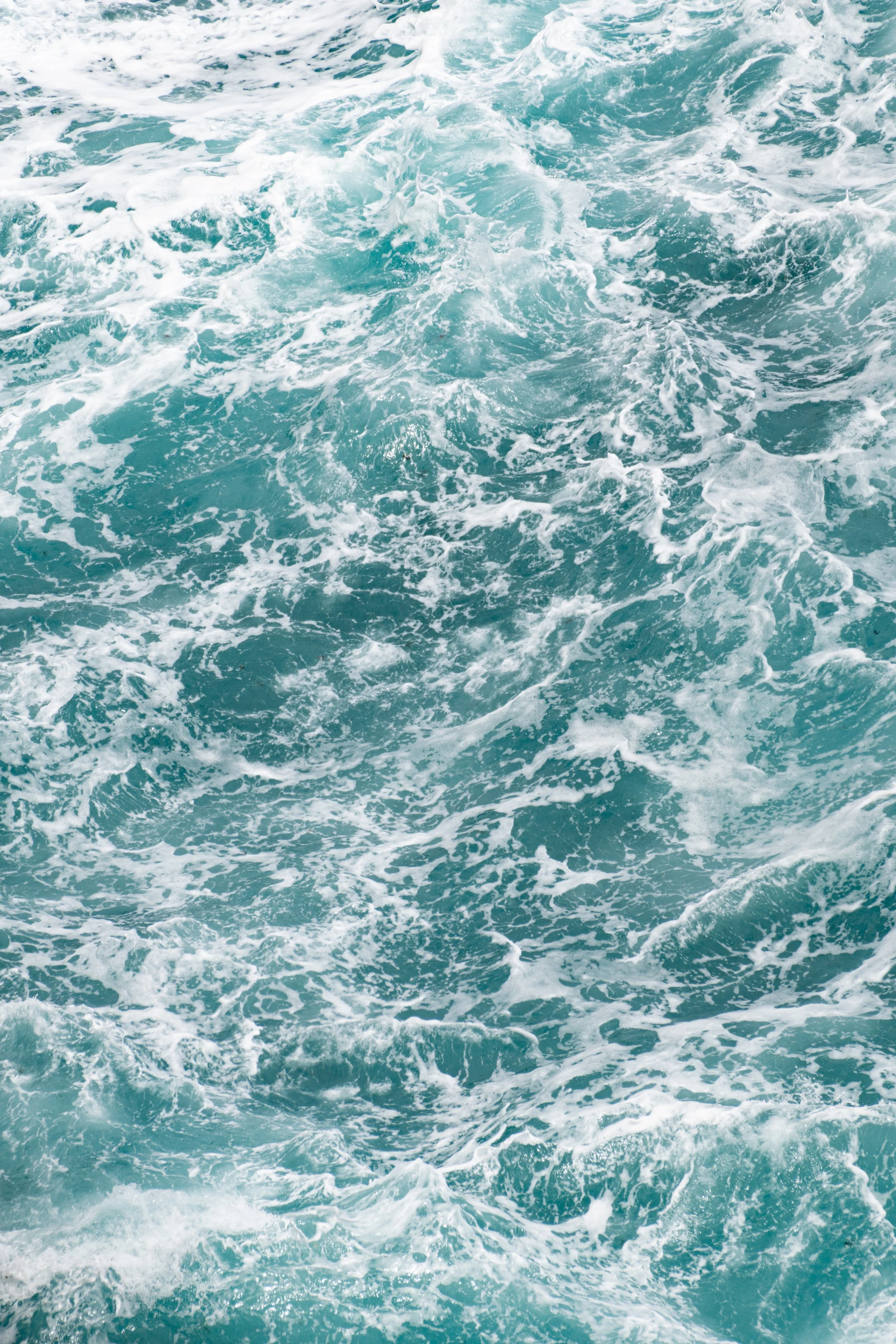 Aerial view of churning blue ocean water with white foam.